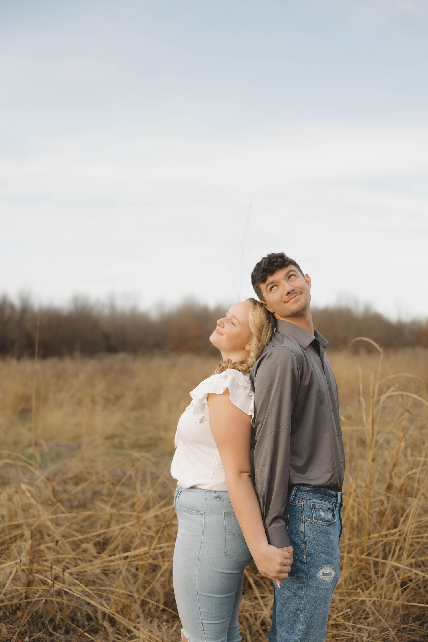A couple shares a tender moment while standing together in a rustic field during golden hour.