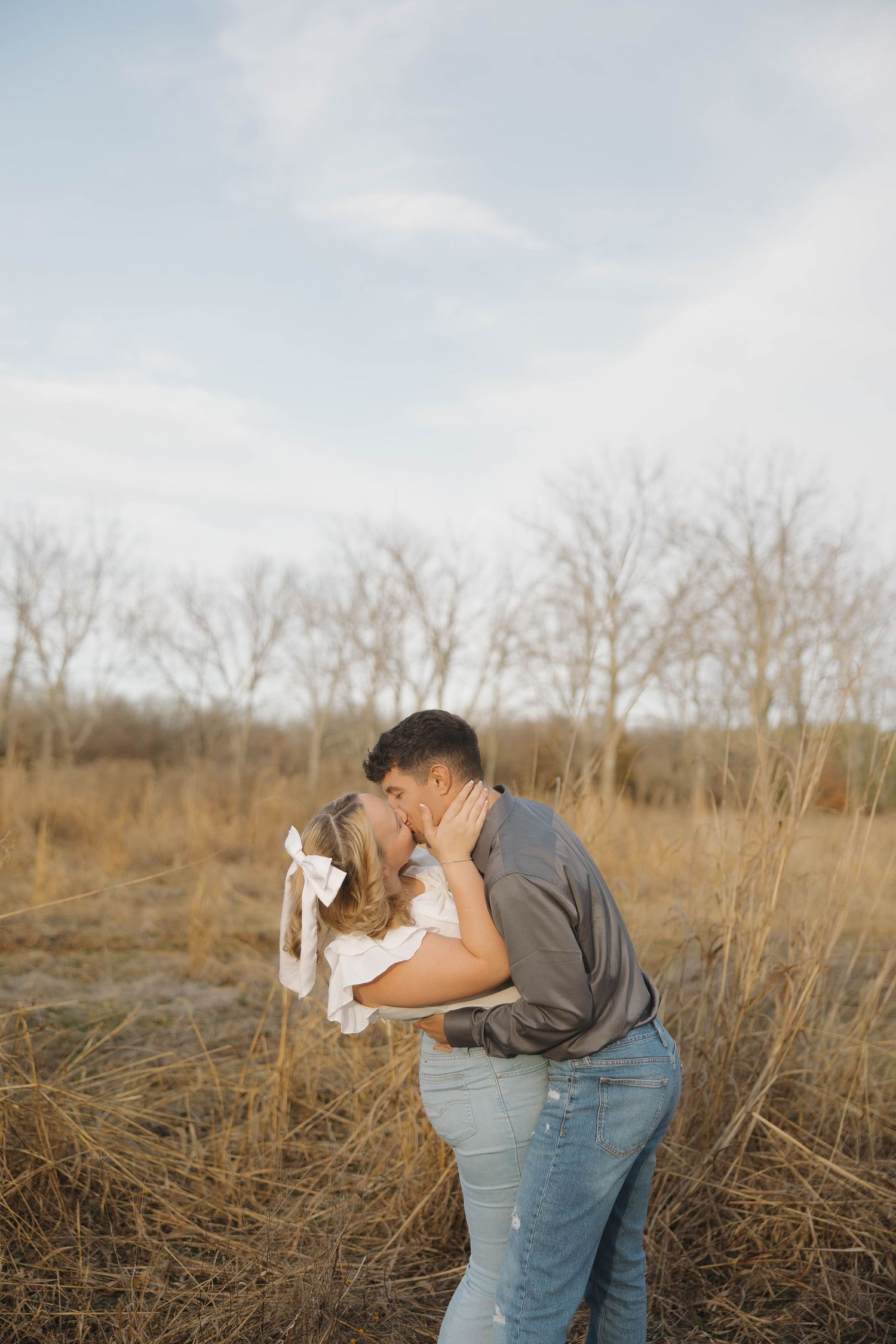 An intimate moment captured between a couple sharing a kiss in a field of tall grass.