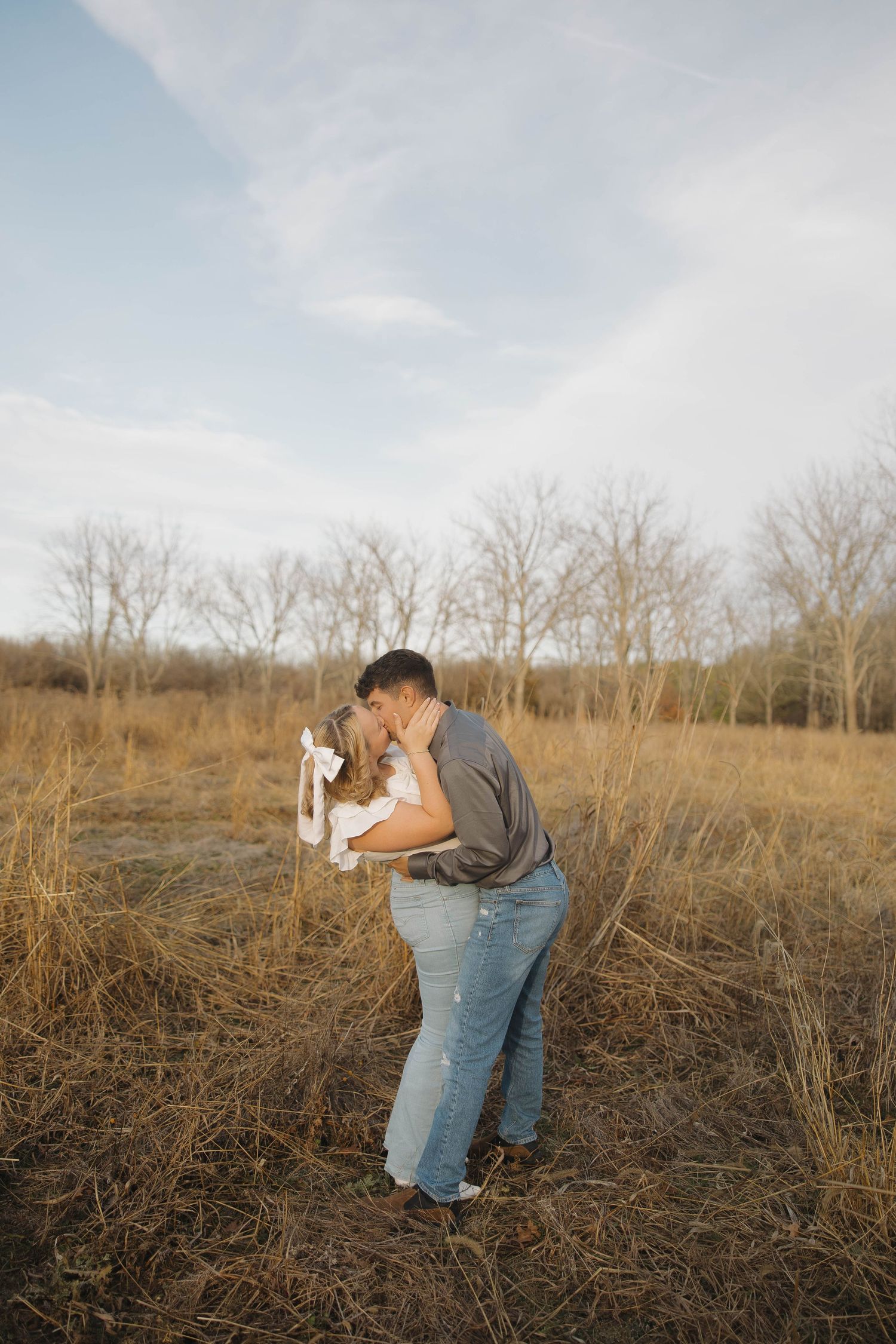 A couple embraces in a romantic moment while standing in a golden field during sunset.