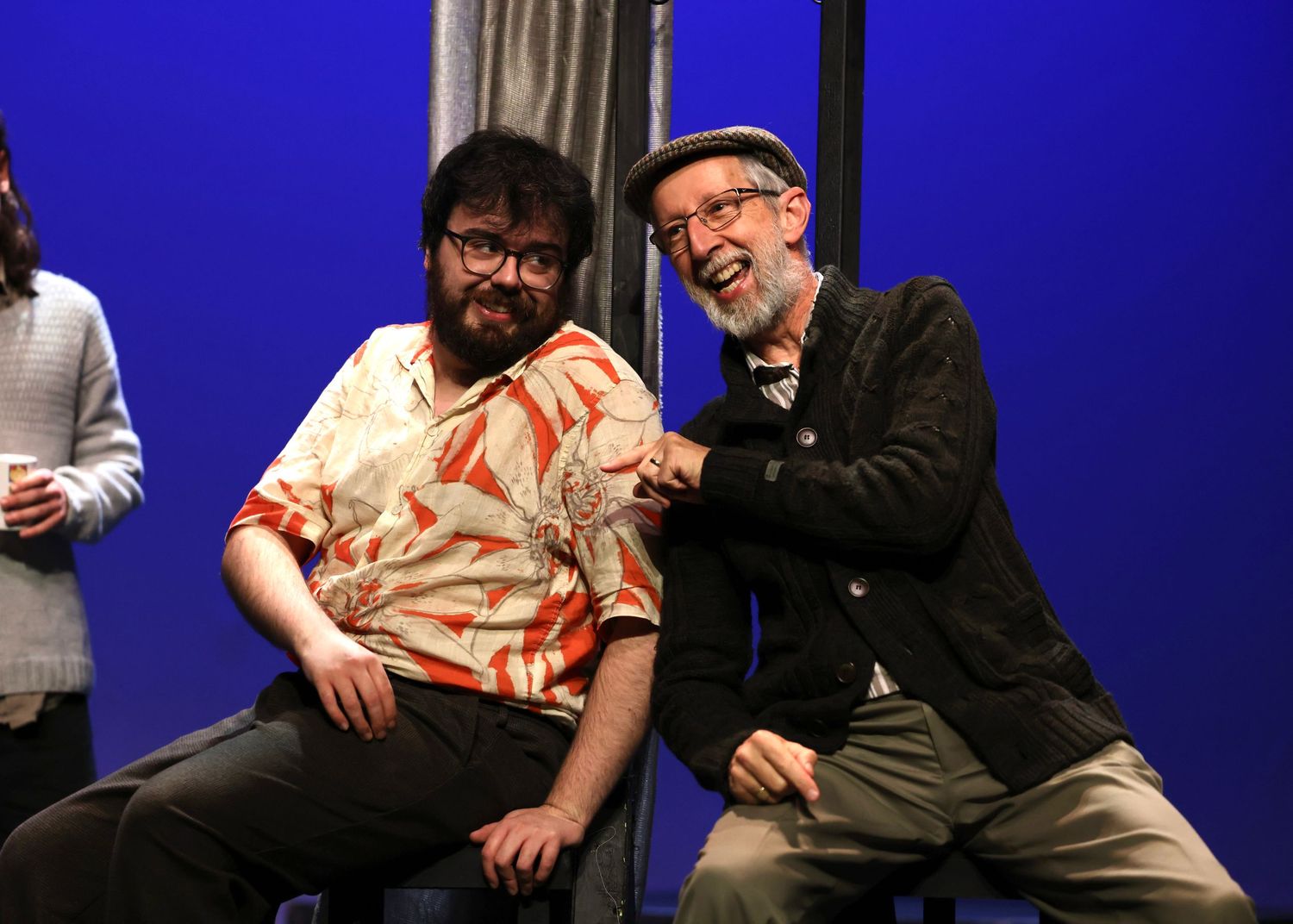 Two people sit together laughing and interacting against a bright blue background.