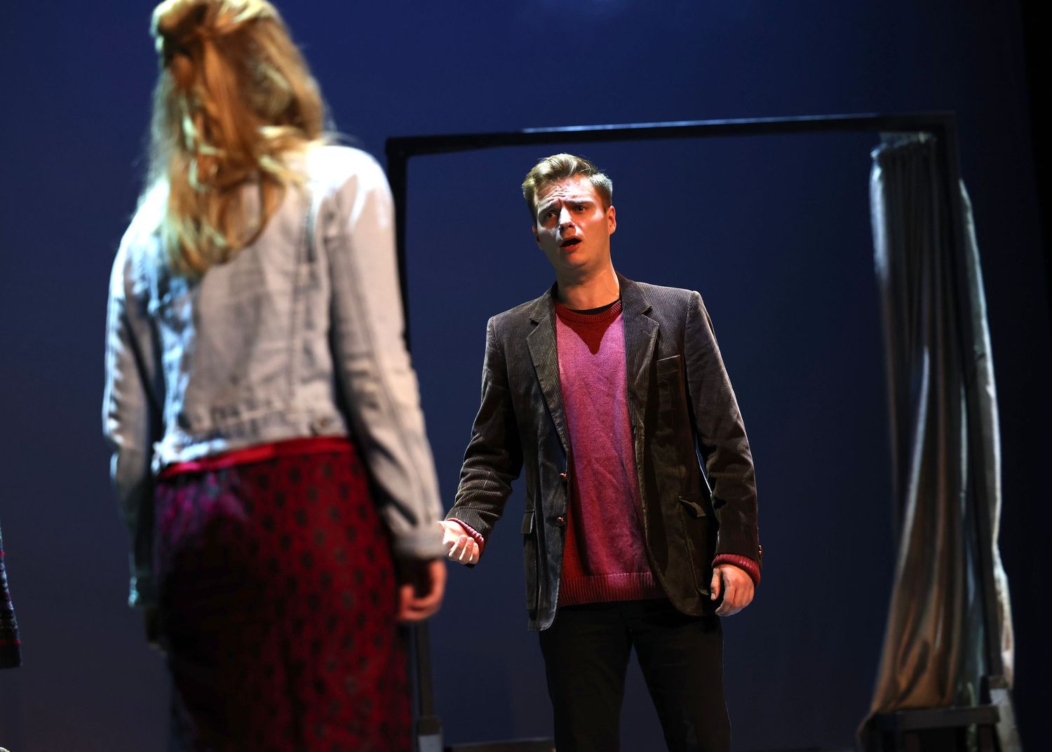 Actors in casual attire rehearsing on dark stage with dramatic lighting.