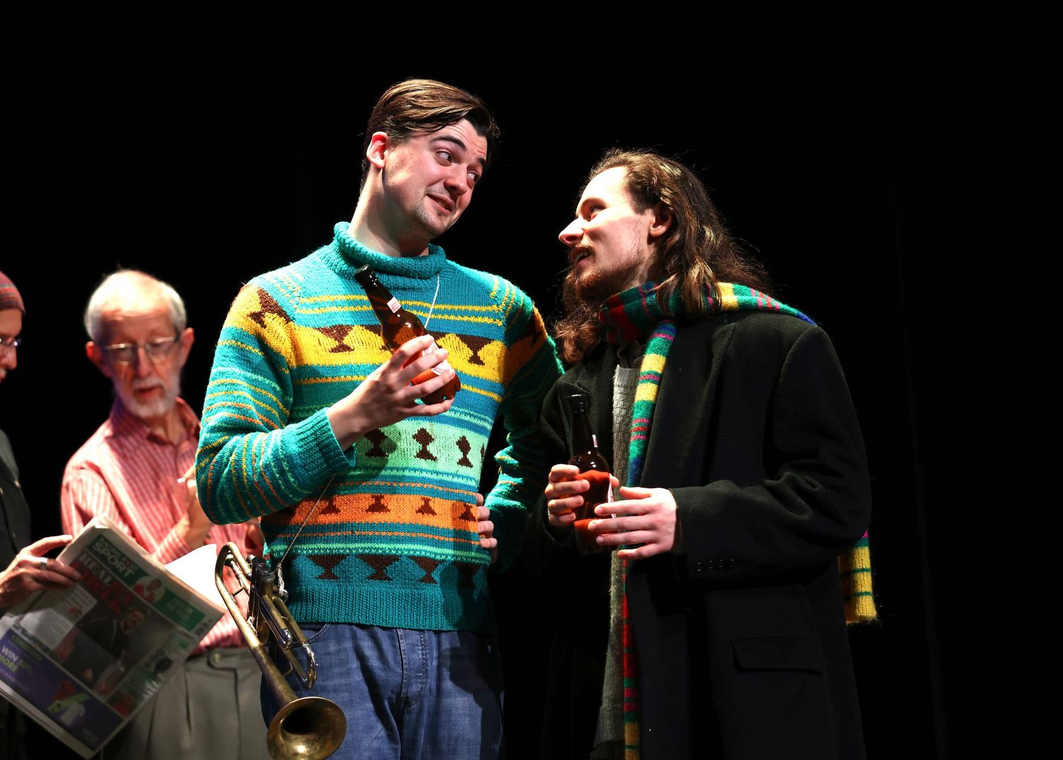 Two performers share a comedic moment on stage while wearing festive sweaters during a theatrical production.