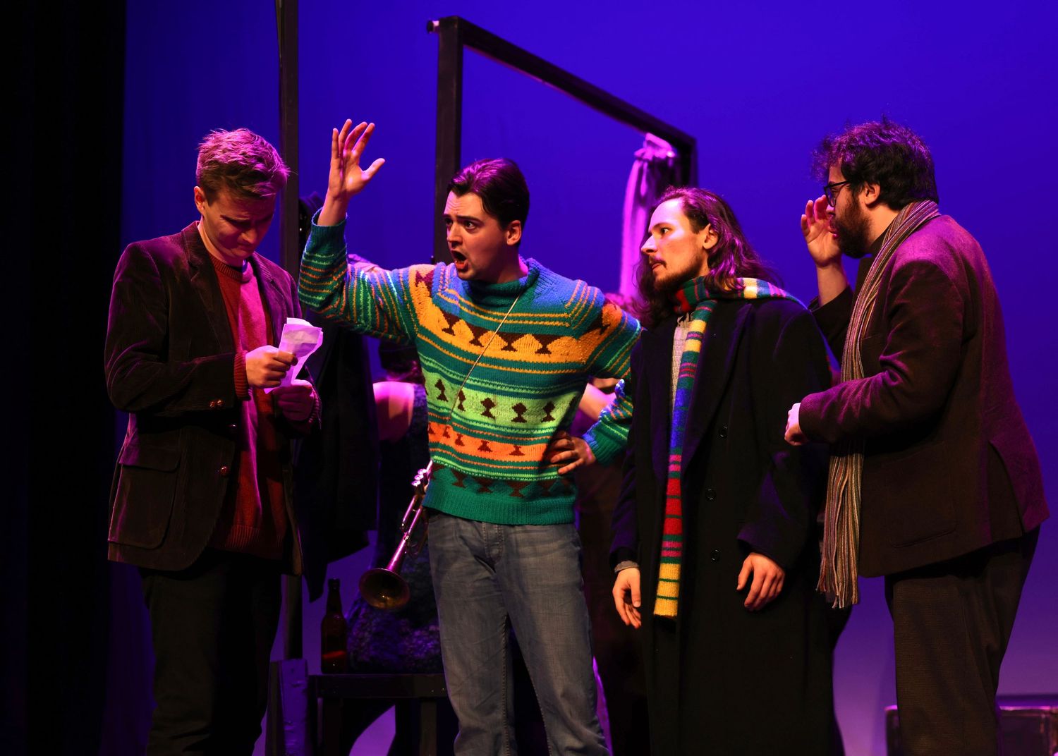 Performers interact on stage during a theatrical production with dramatic blue and purple lighting effects.