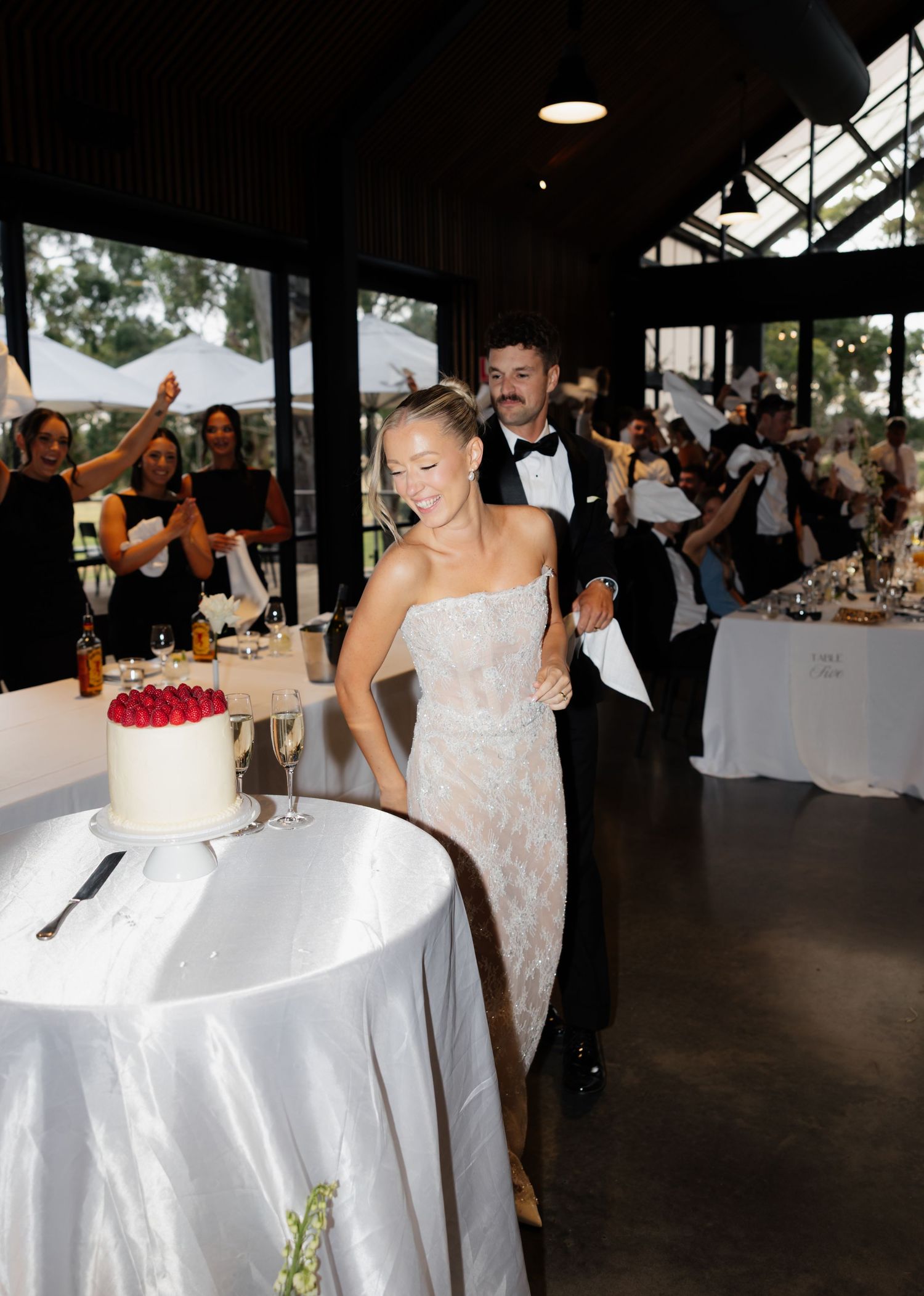 Wedding reception celebration with guests dining and dancing in an indoor venue with white tablecloths.