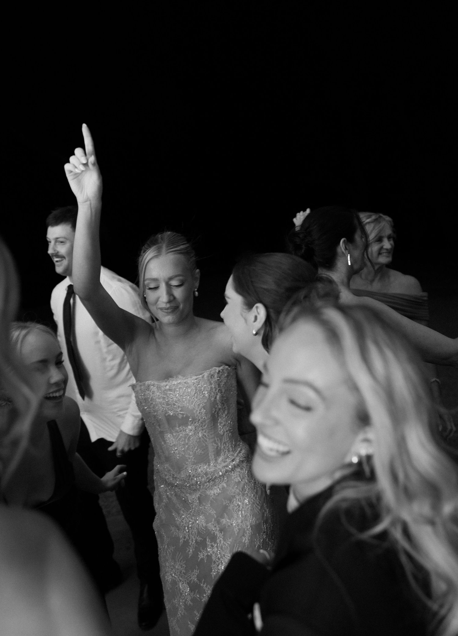 Wedding party guests dancing and celebrating in black and white on a dark dance floor.