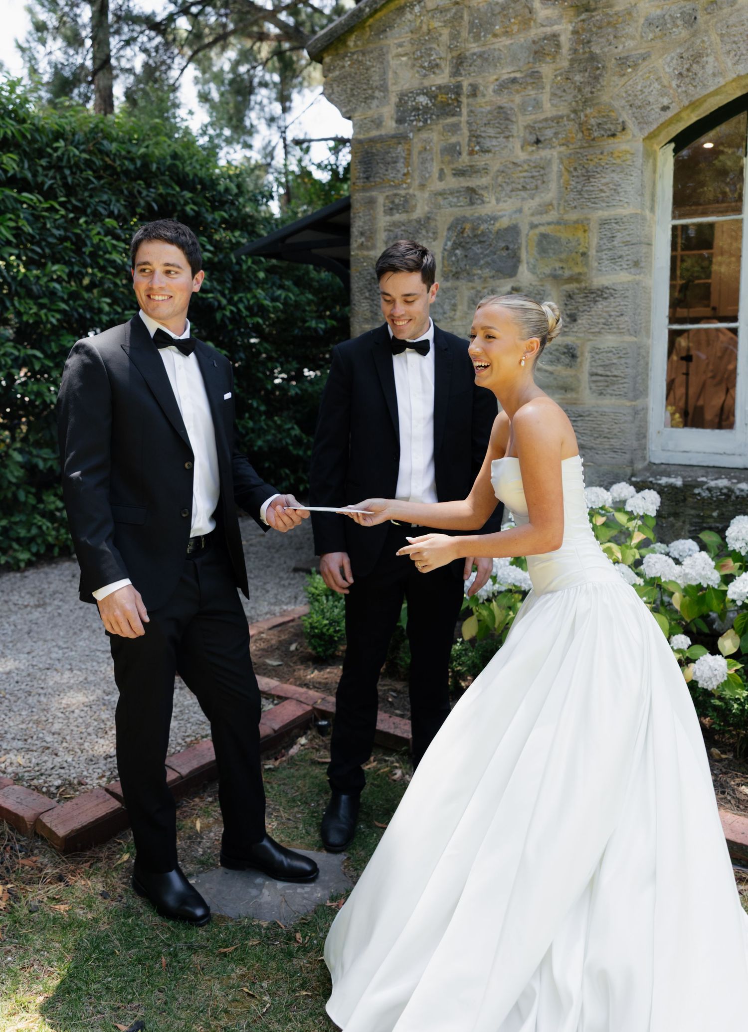 A series of candid wedding moments captured outside a rustic stone building with white flowers.