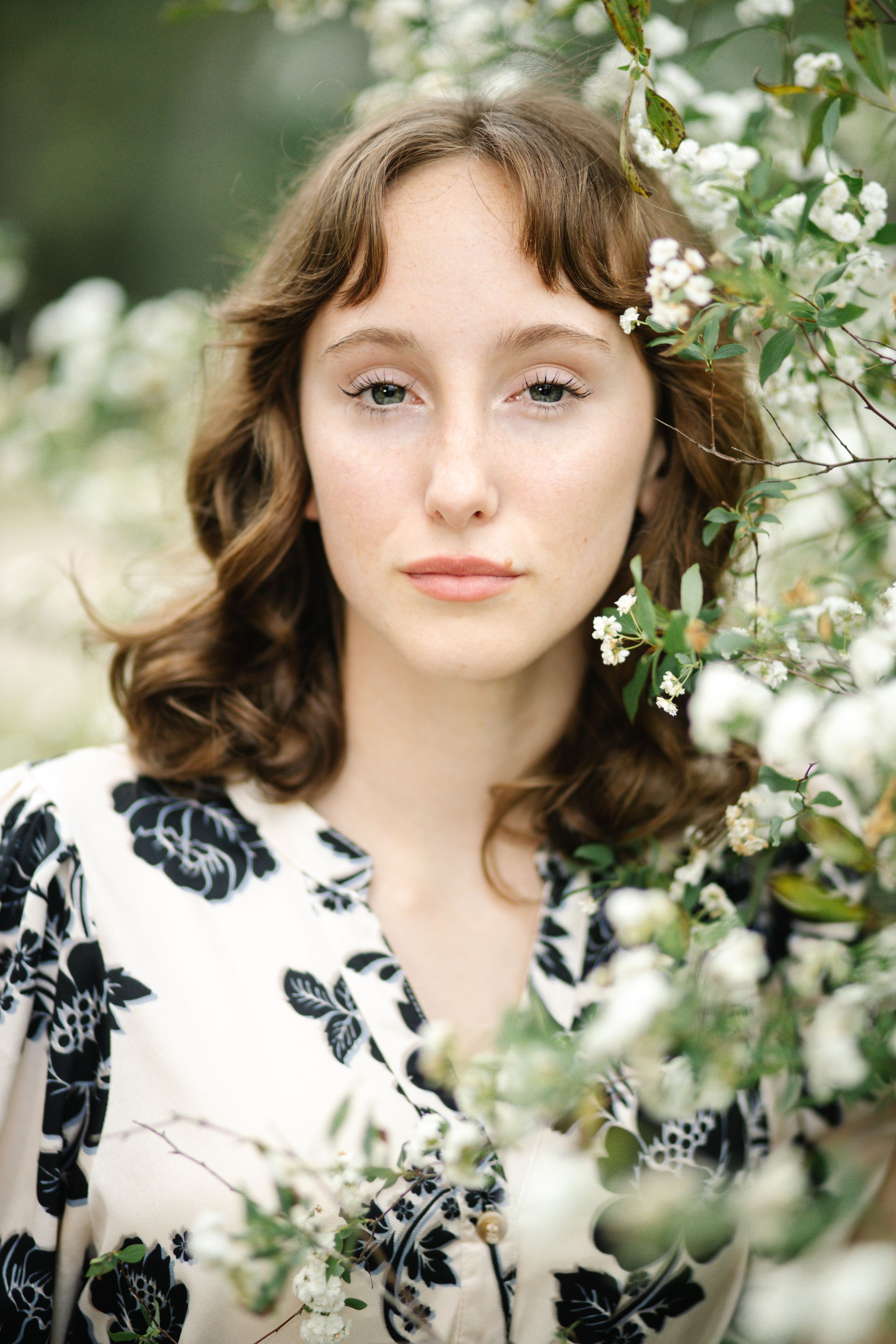 A series of portraits showing someone in a black and white floral dress posing among blooming white spring flowers.