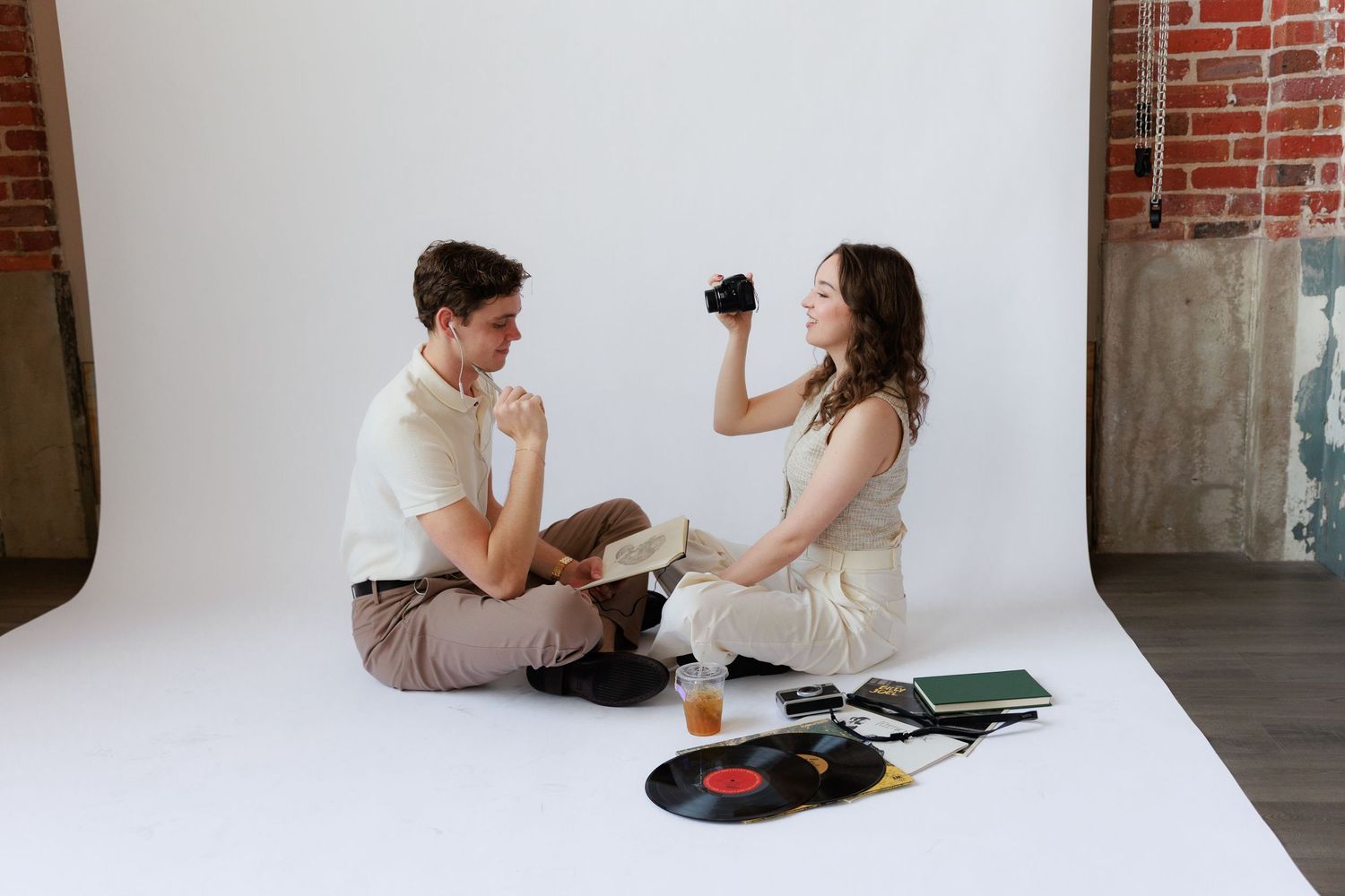 Two people sit on floor having fun with vinyl records and drinks in modern loft apartment setting.