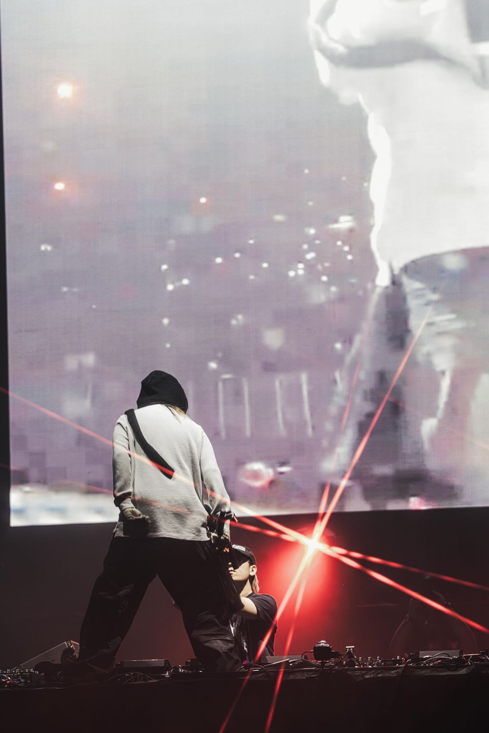 Electronic music performer in white hoodie using red lasers and fog effects during dramatic nightclub performance.