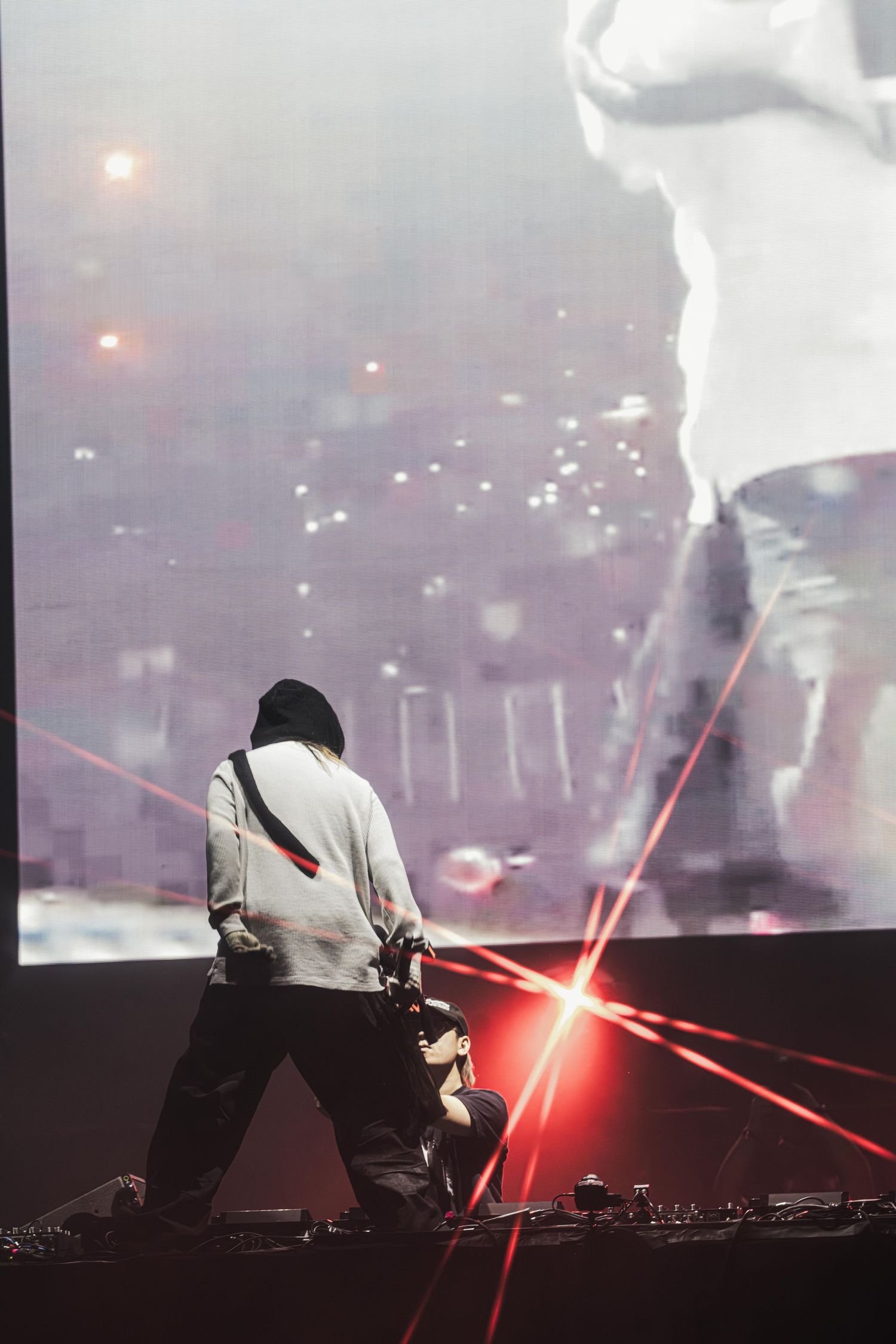 Electronic music performer in white hoodie using red lasers and fog effects during dramatic nightclub performance.