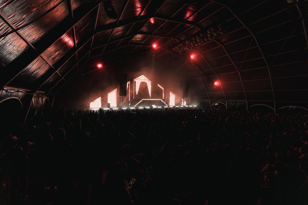 Red lights illuminate a dark industrial space with metal beams and architectural details creating a moody atmosphere.