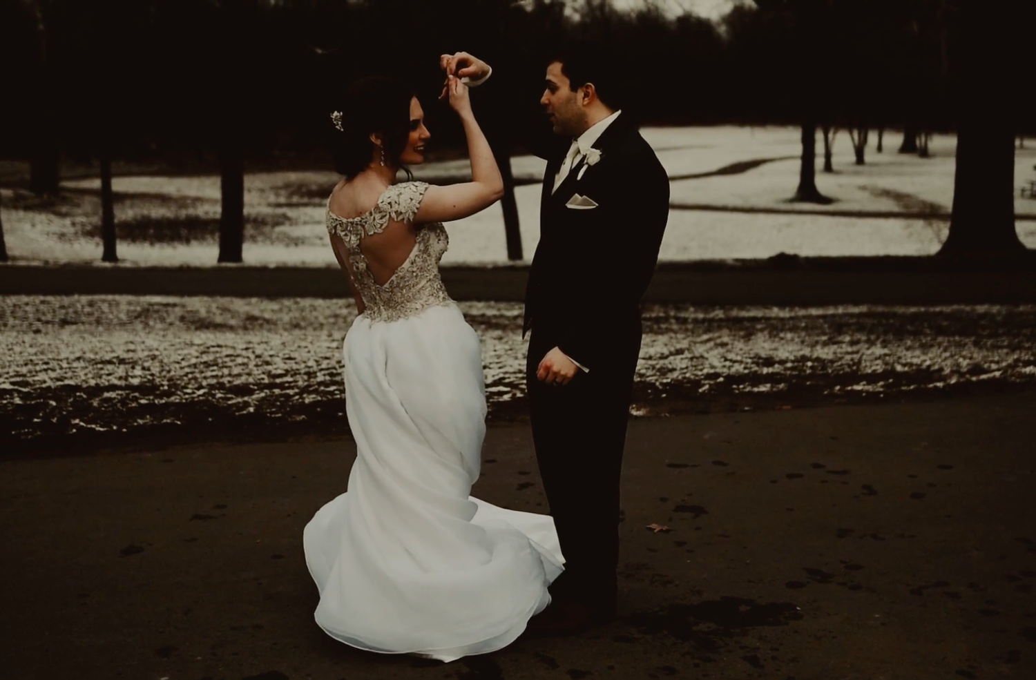 A couple in wedding attire dances together on a beach during sunset creating a romantic silhouette.