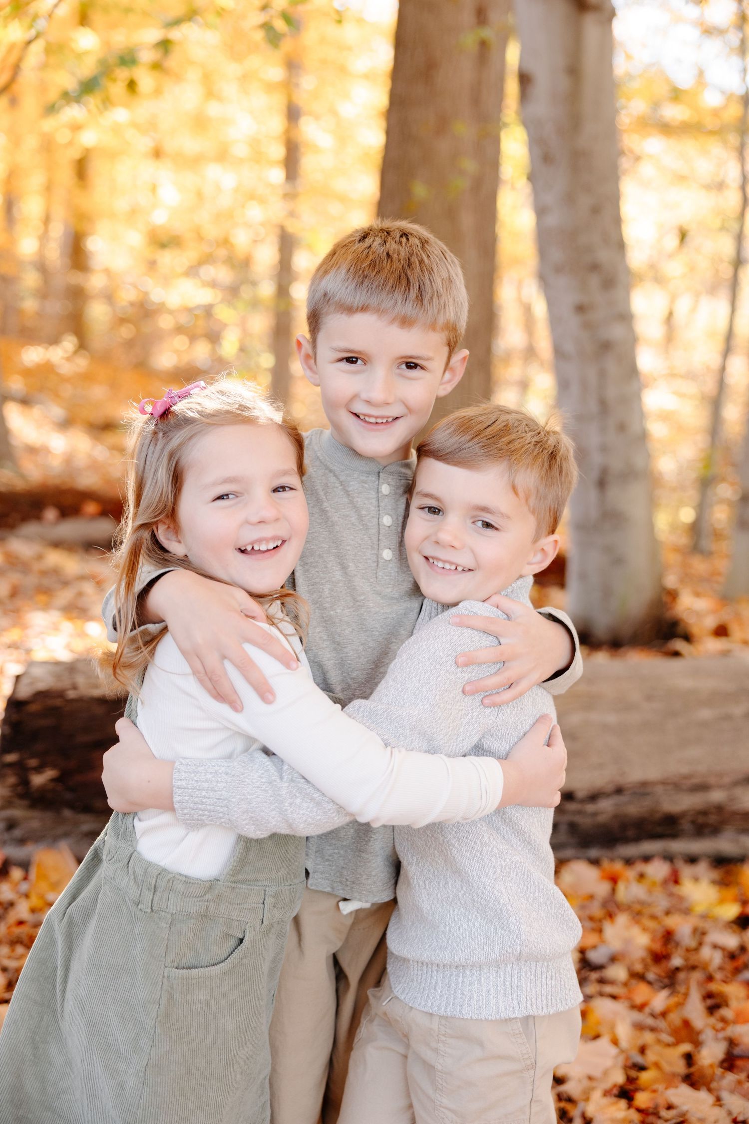 Two children hugging and smiling while playing in autumn forest with fallen leaves.