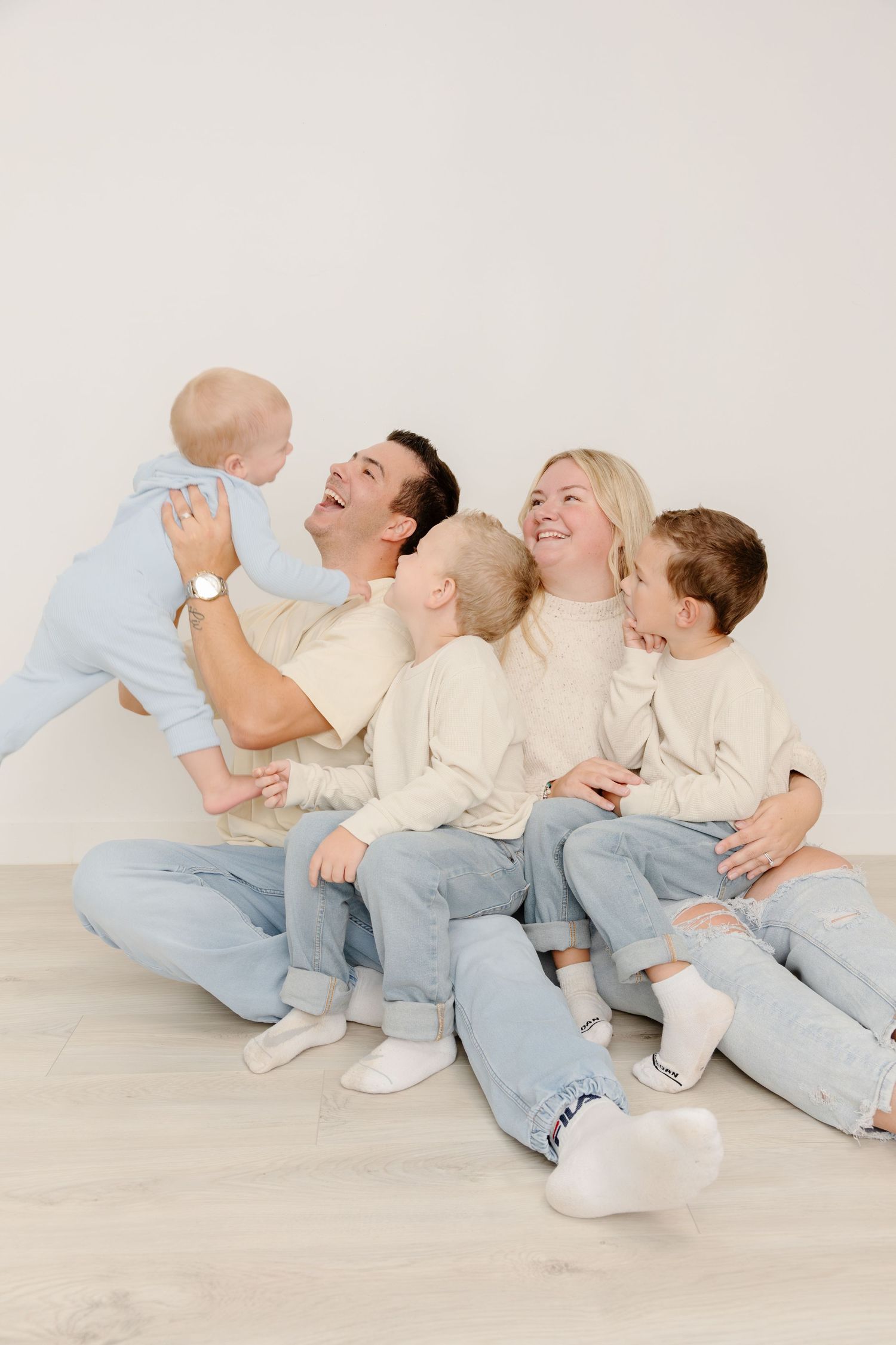 A playful sequence of family members in white shirts and jeans laying on the floor in a domino effect pose.