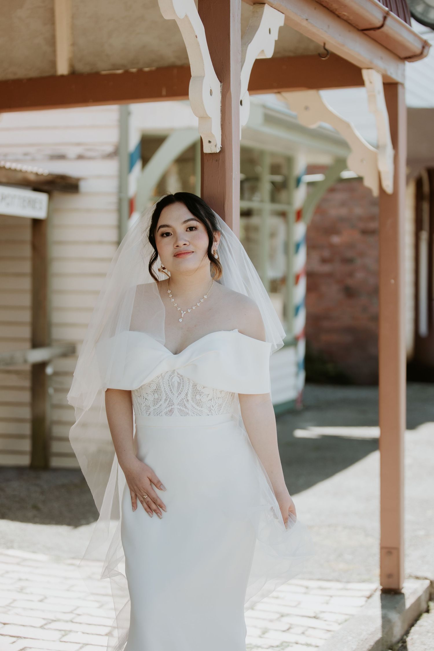 A bride in a white wedding dress poses on a porch with white columns and natural lighting.