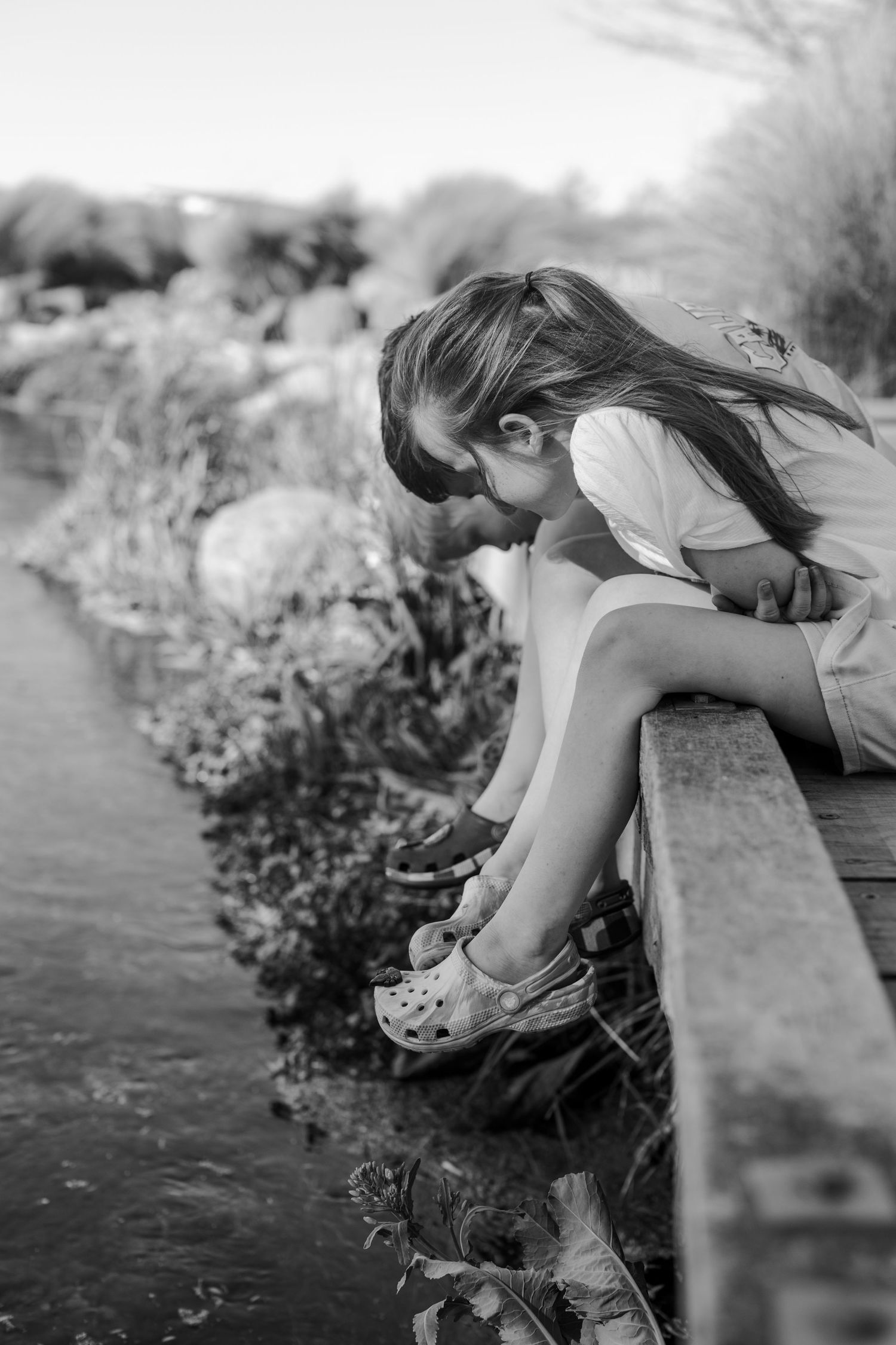 A series of black and white photographs showing someone leaning over water's edge with flowers in a dreamy artistic style.