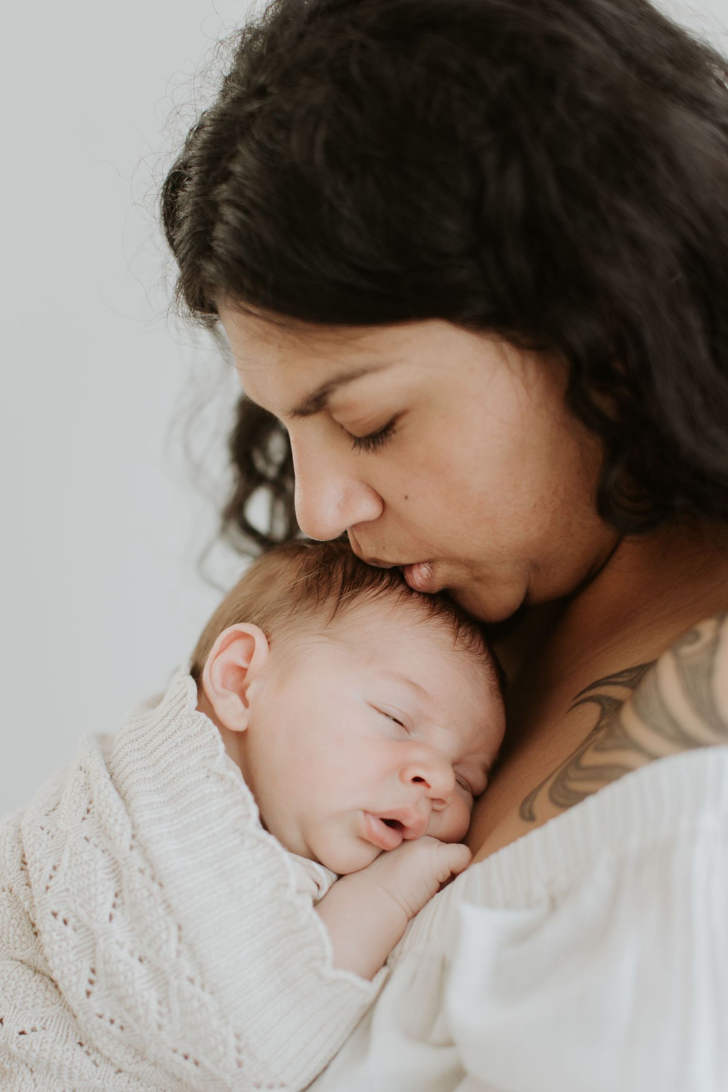 A tender moment captured in black and white as a parent and baby share a peaceful embrace on white bedding.