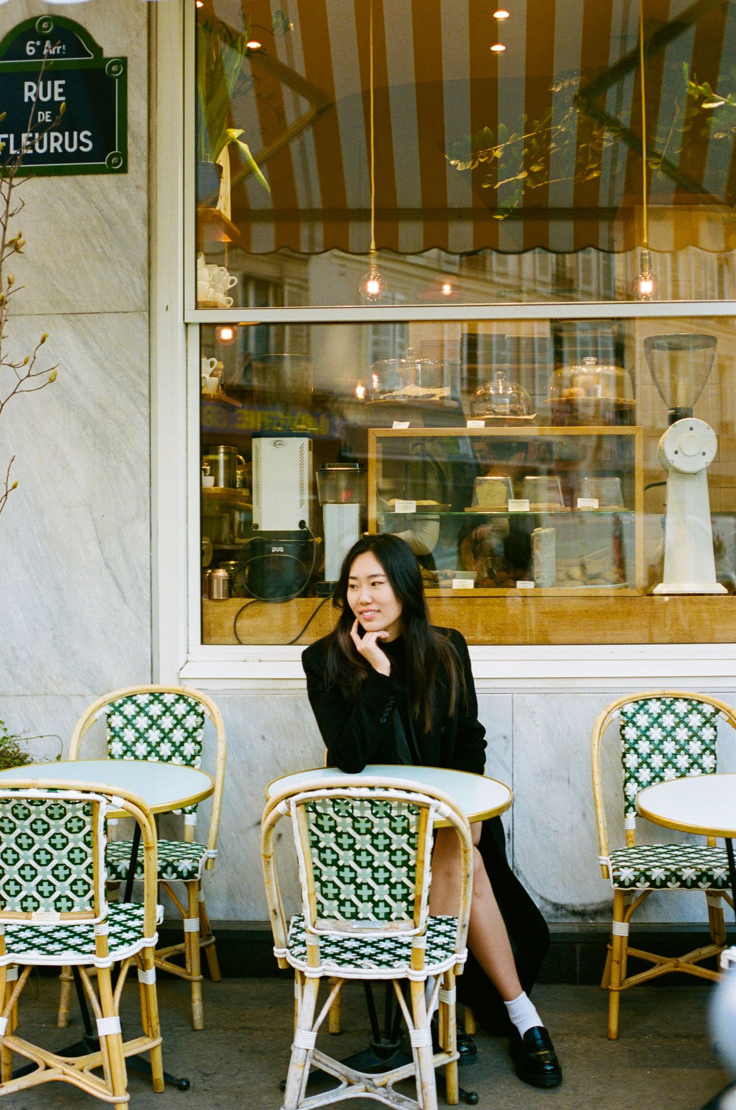 A bistro table and woven rattan chairs outside a quaint Parisian cafe on Rue de Fleurus with warm lighting in the window.