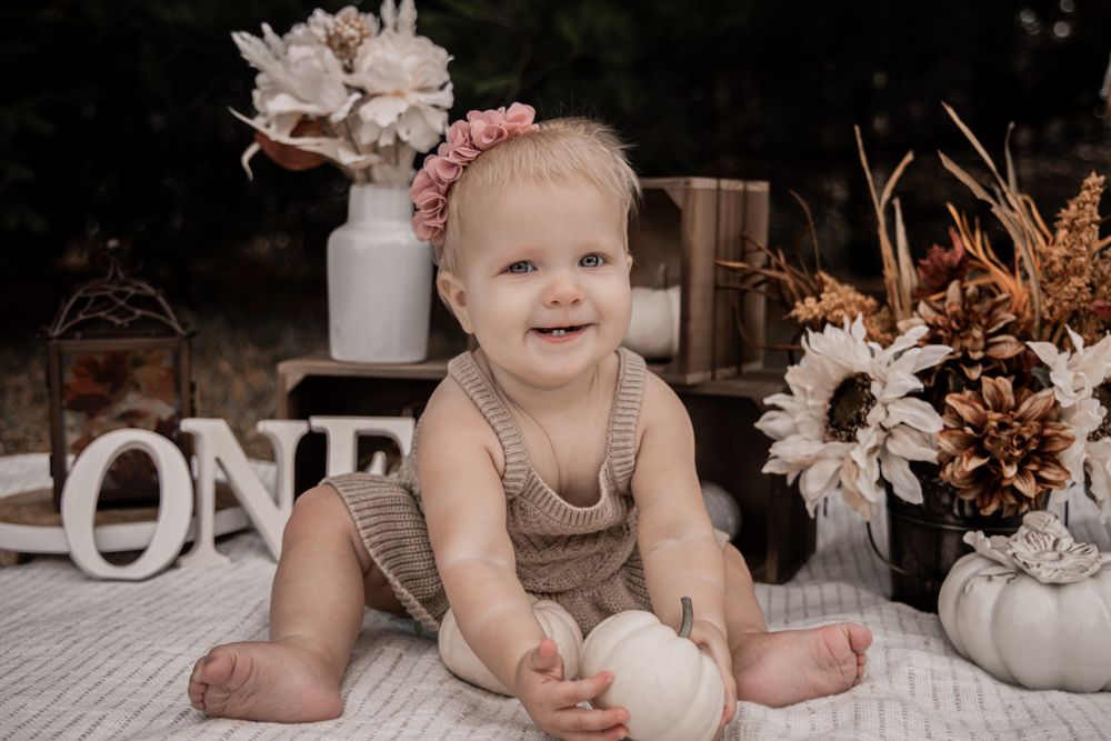 First birthday photoshoot setup with autumn decorations and a smiling baby in beige clothing.