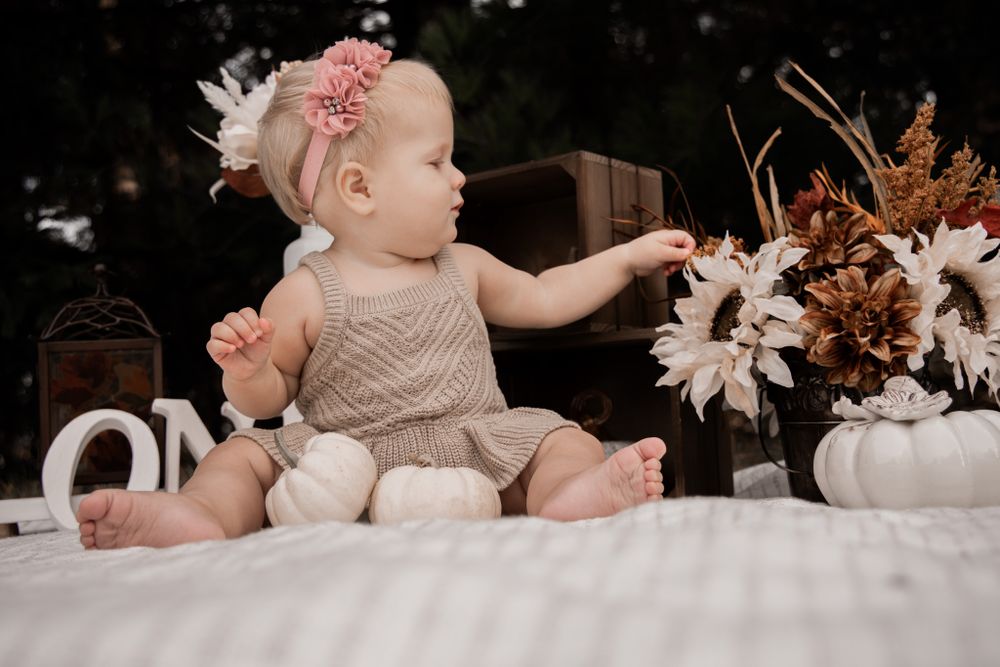 Baby in beige clothing reaches toward floral decorations during first birthday photoshoot.