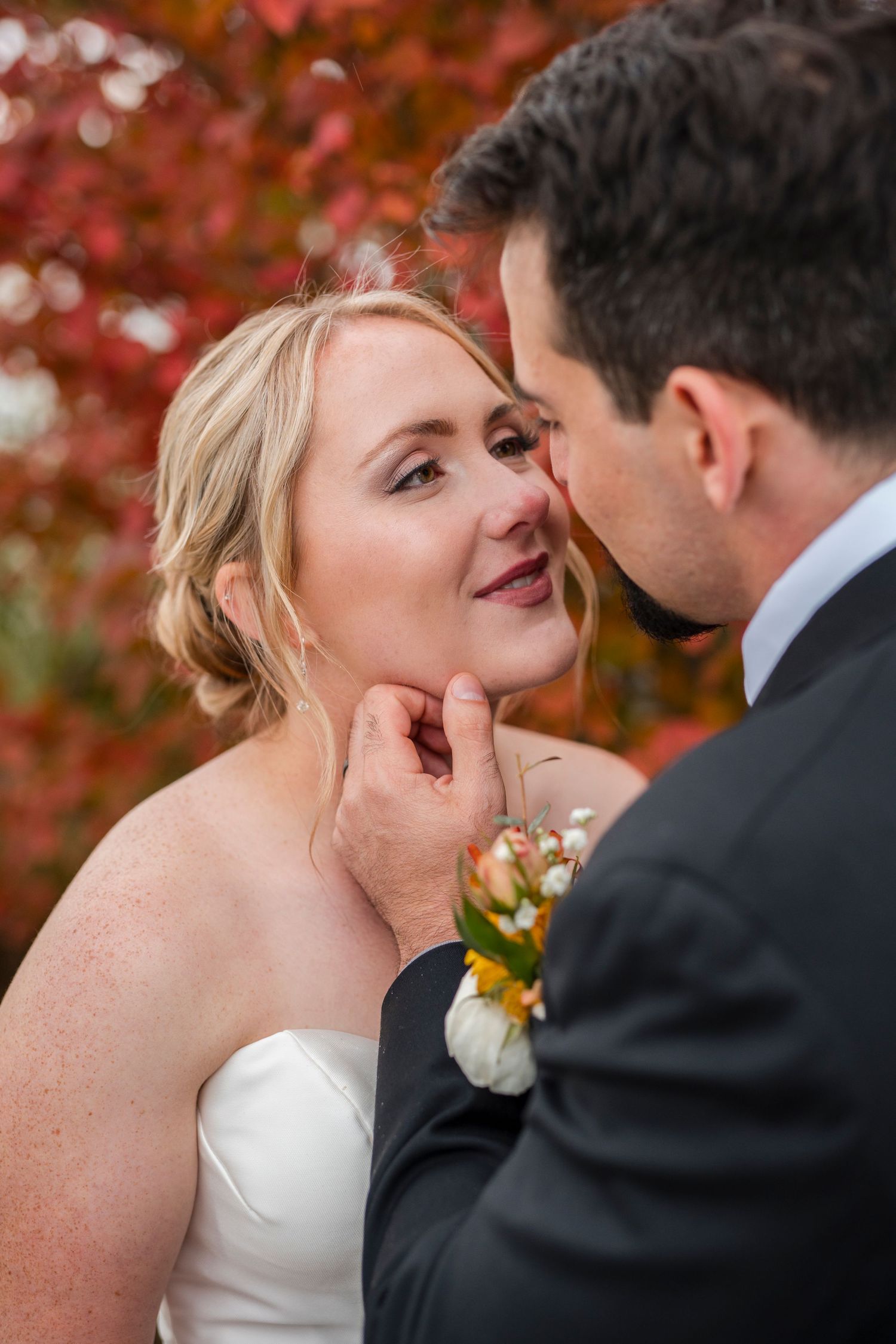 Wedding couple sharing an intimate moment against vibrant red autumn foliage.