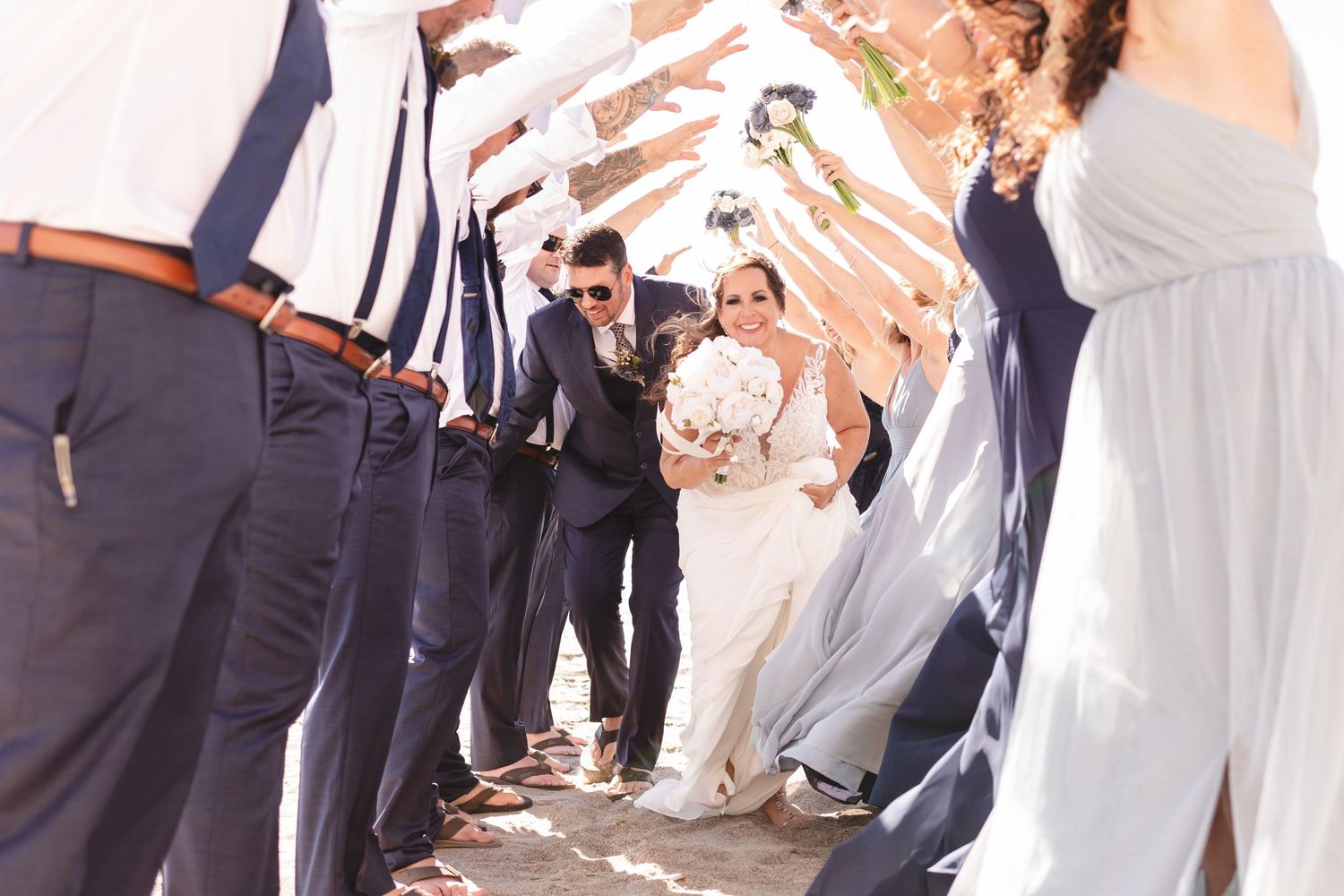 Wedding party forms tunnel archway for newlyweds walking through.