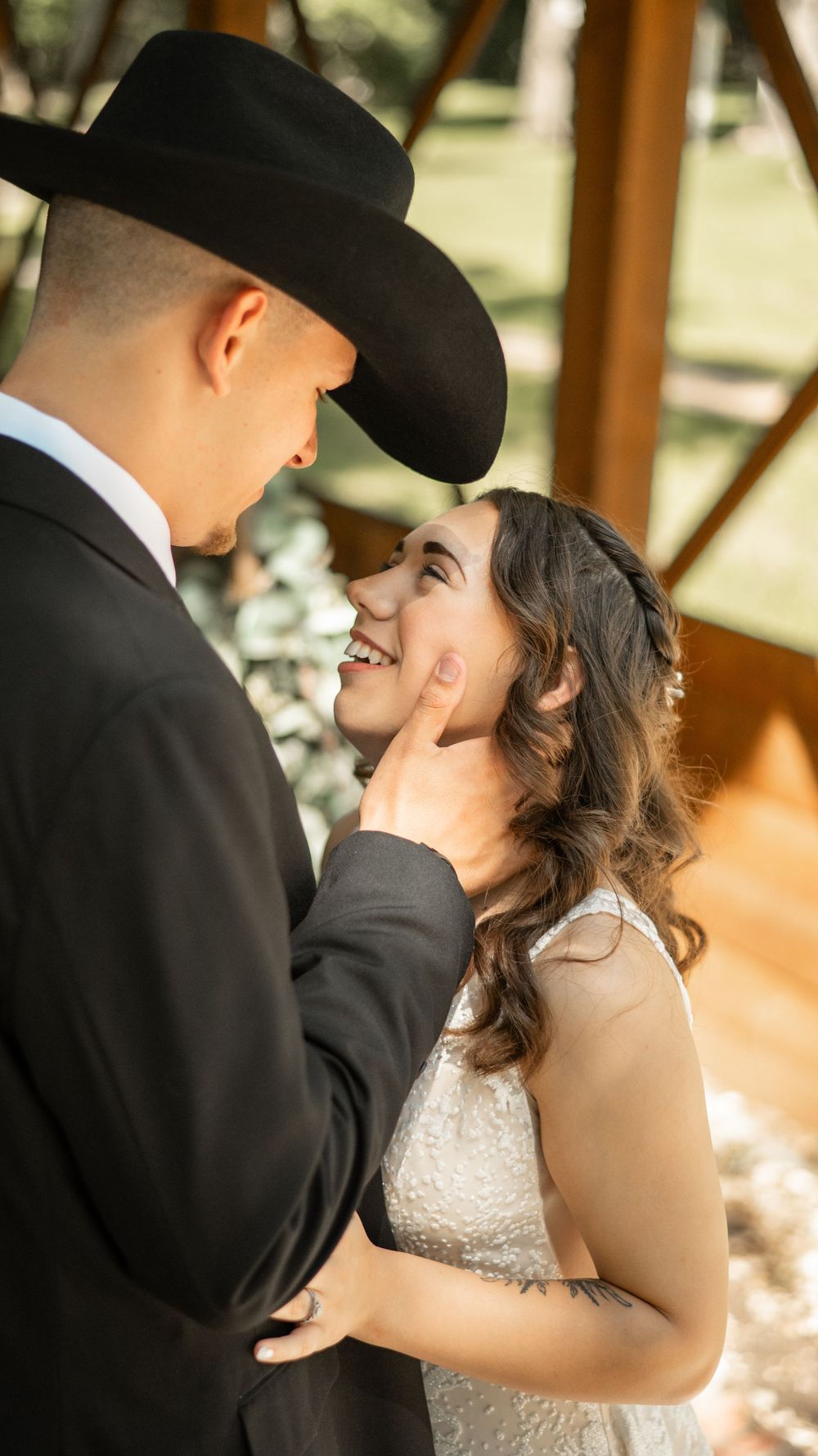 A tender moment between newlyweds as a groom in a black cowboy hat gazes at his bride in a white lace dress.