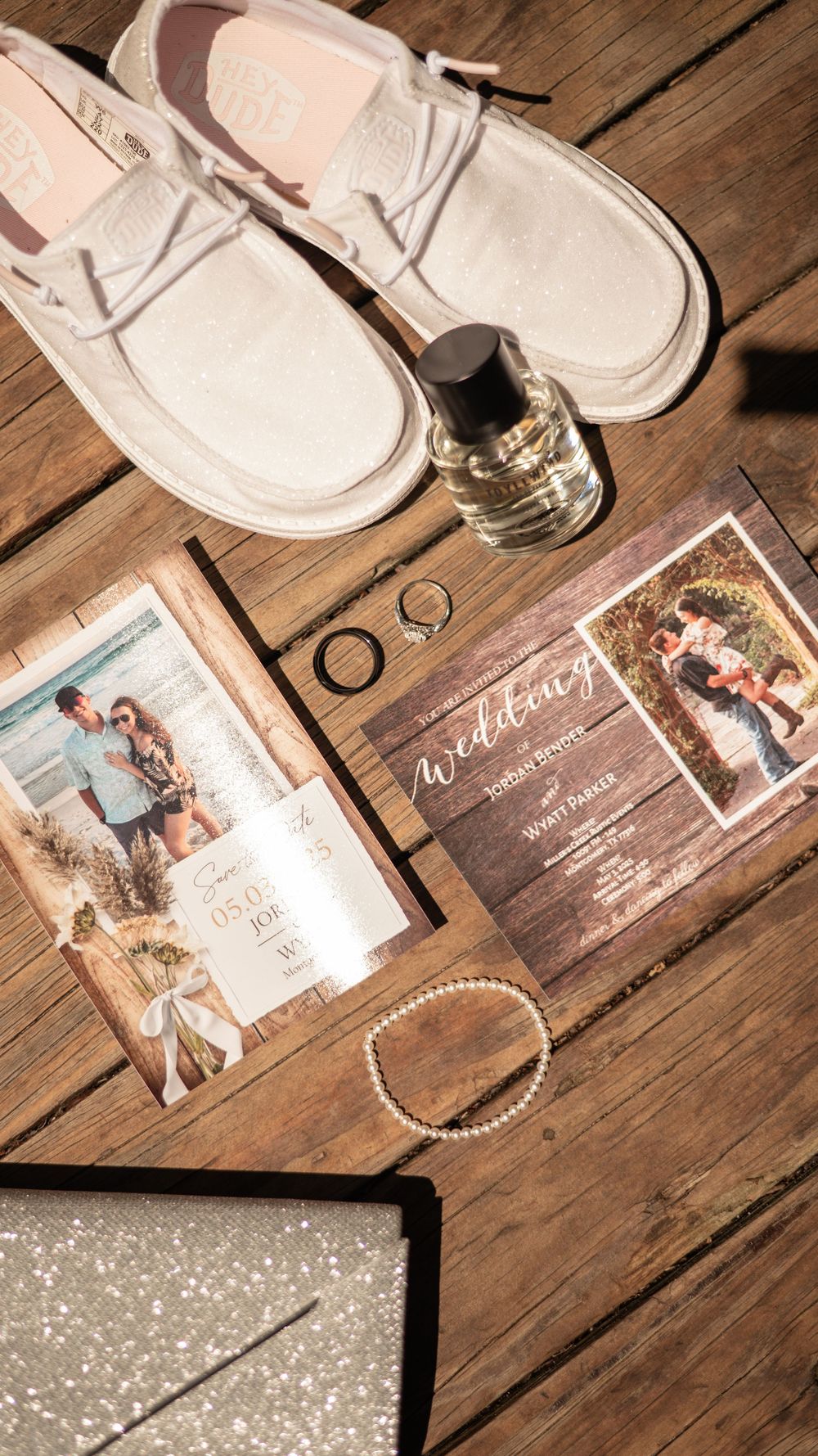 Wedding invitations and photographs arranged with white shoes on a rustic wooden deck floor.