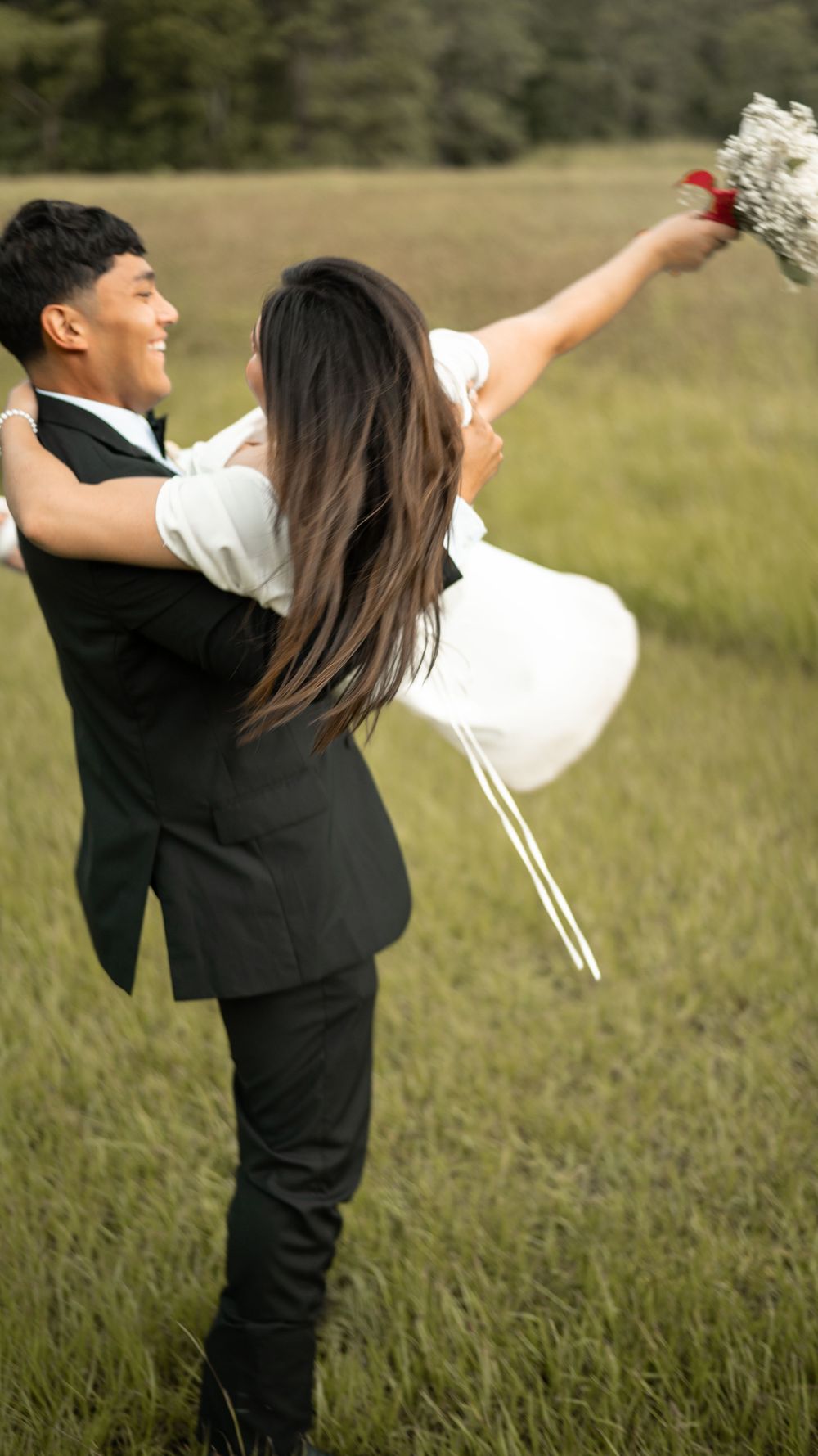 Two people in formal attire dance playfully in a grassy meadow at sunset creating a romantic silhouetted scene.