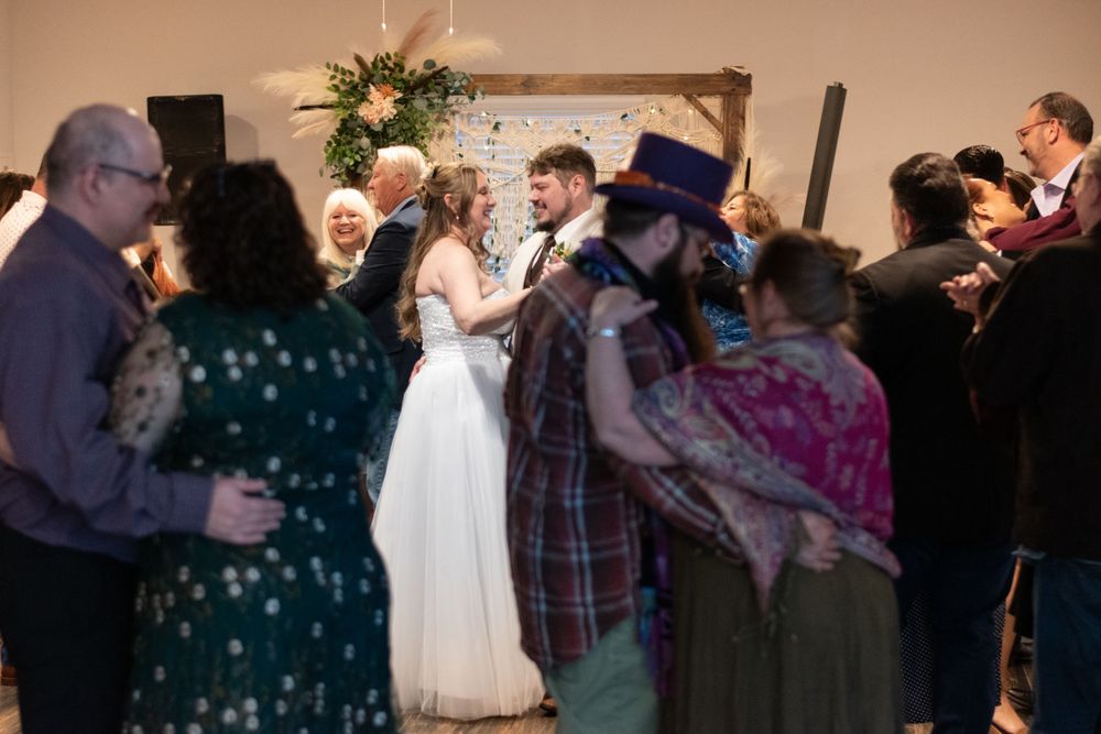 Wedding guests dance together in a circle around the newlyweds at an indoor reception venue.