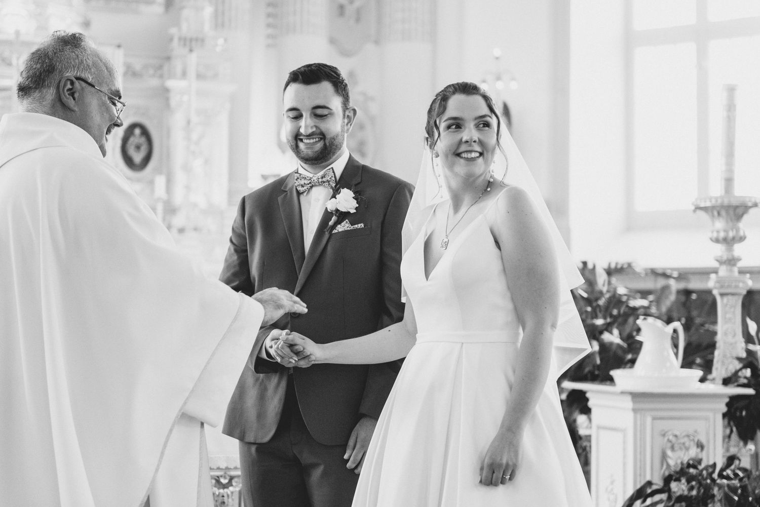Black and white wedding ceremony photo showing a joyful couple sharing a moment with an officiant at the altar.