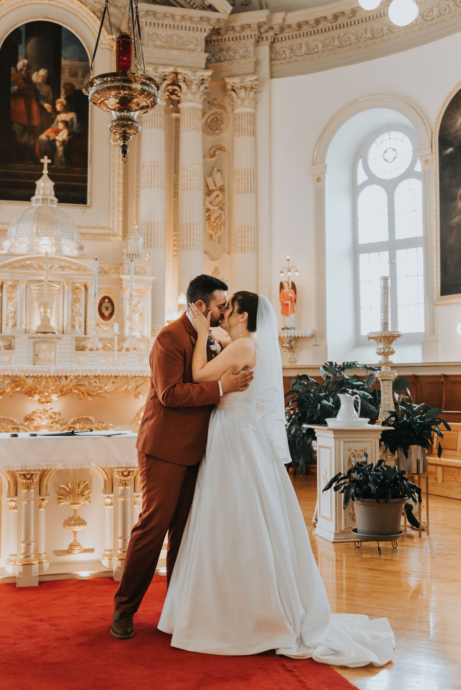 A romantic wedding moment in an elegant church interior with classical architecture and red carpet.