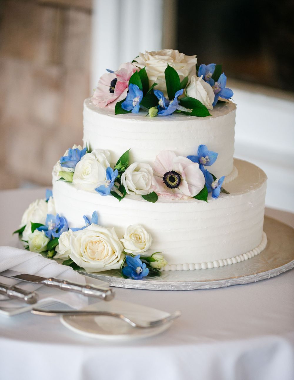 Two tiered white wedding cake adorned with fresh flowers in blue and white.