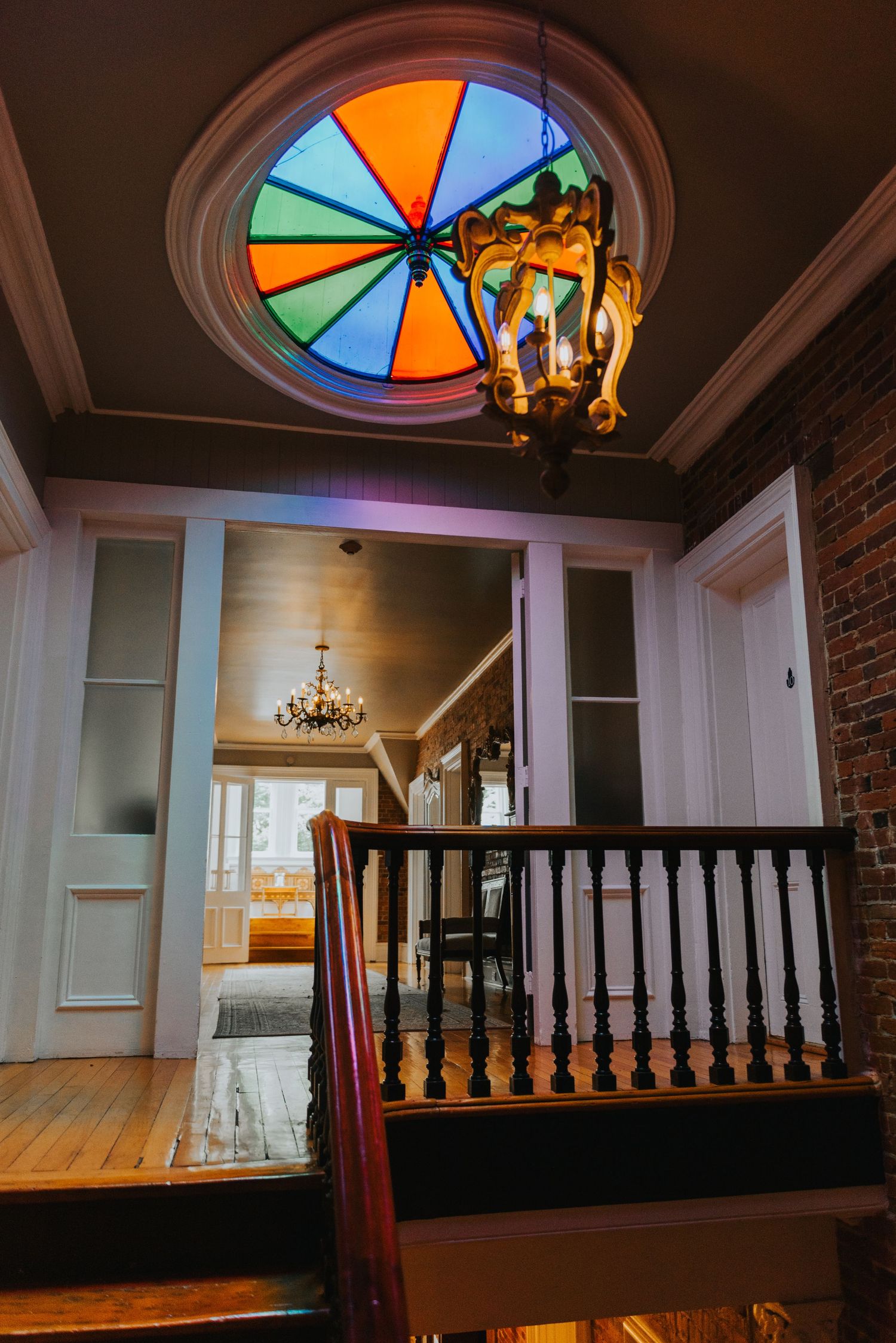 Interior staircase with stained glass round window and vintage chandelier in historic home features wooden railings and warm lighting.