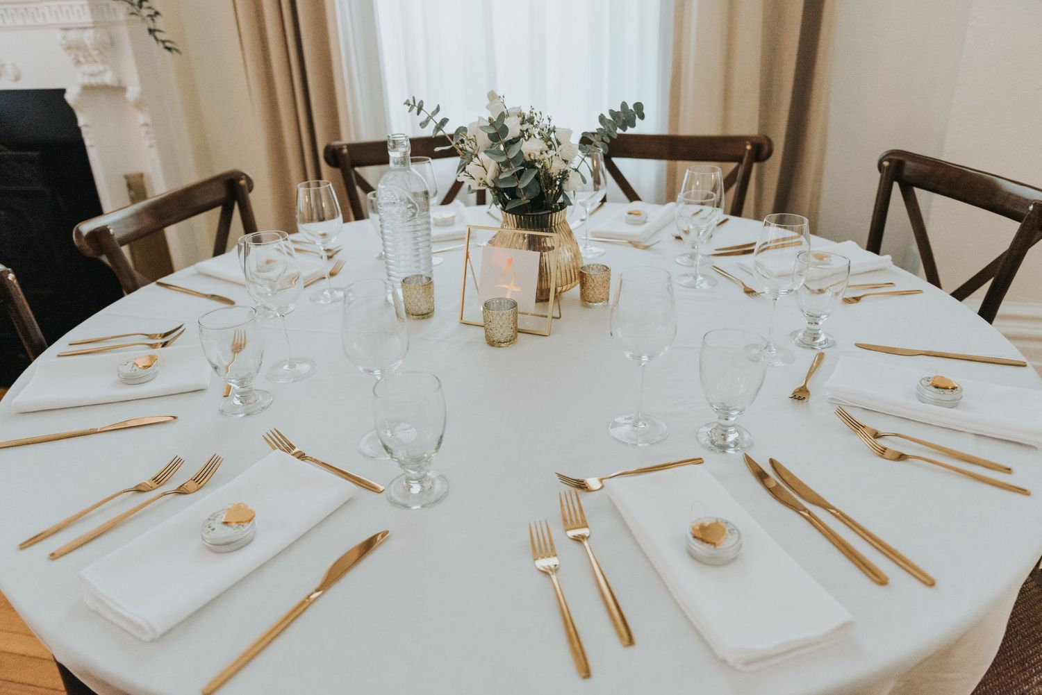 Elegant round dining table set with white linens, gold flatware, and simple greenery centerpiece for a minimalist wedding reception.