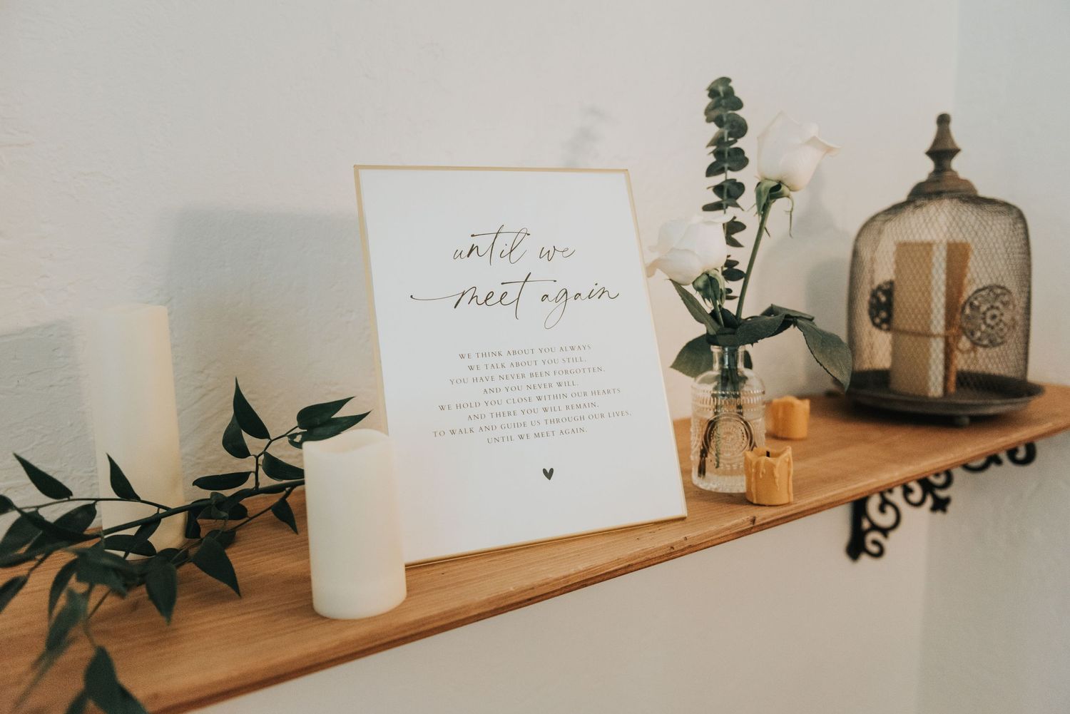 Minimalist shelf styling with eucalyptus, candles, and framed quote on wooden floating shelf against white wall.