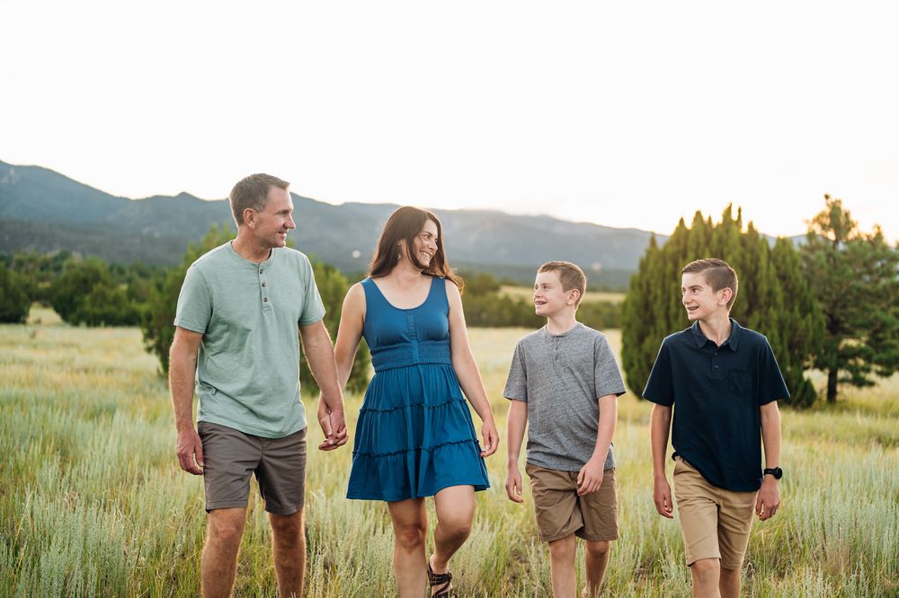 A family walks together through a scenic mountain meadow at sunset holding hands.