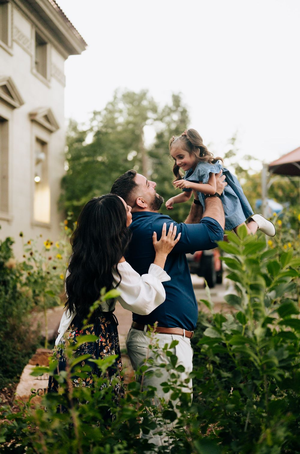 A loving family shares a joyful moment together in a garden setting outside a building.