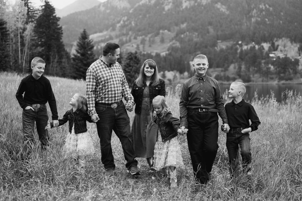 A black and white photo series showing a family walking together through a scenic mountain meadow landscape.