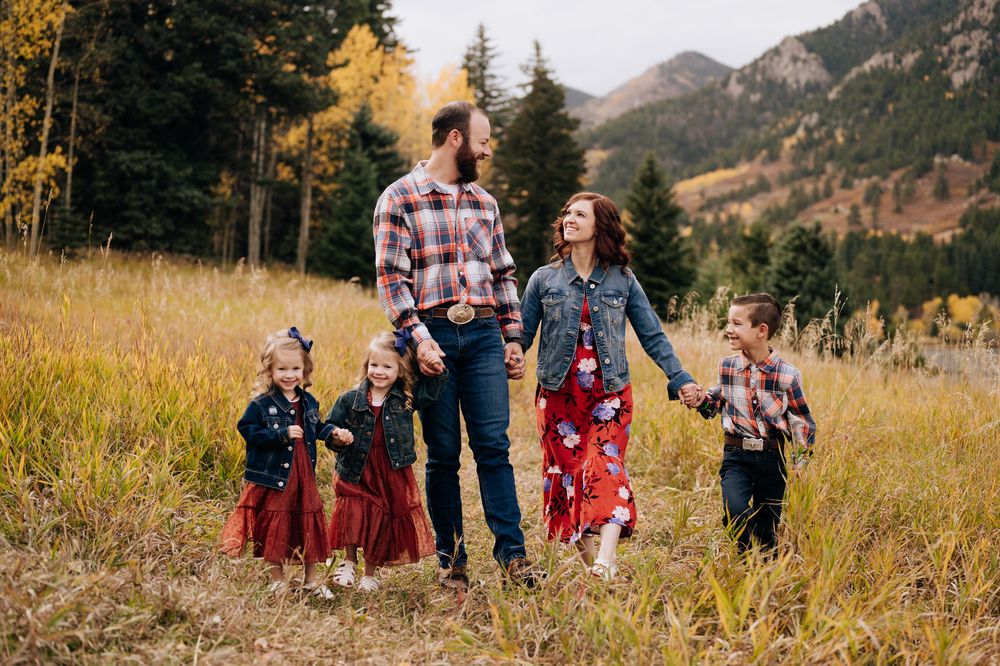 A group stands in a scenic mountain meadow with golden grass and evergreen trees in the background during autumn.