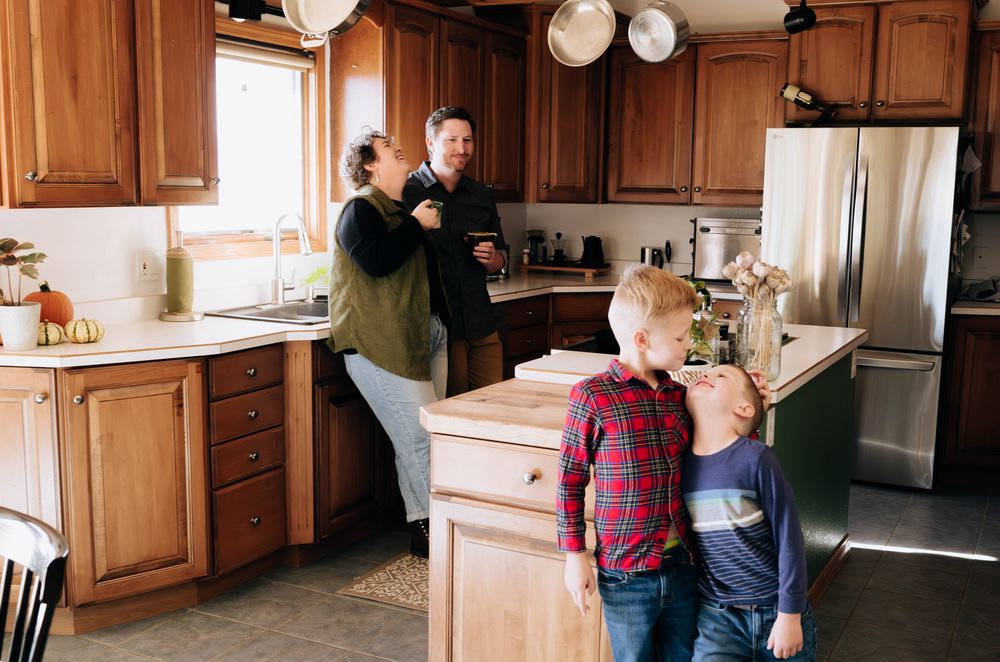 People gather in a modern kitchen with wooden cabinets and natural lighting during a social event or gathering.