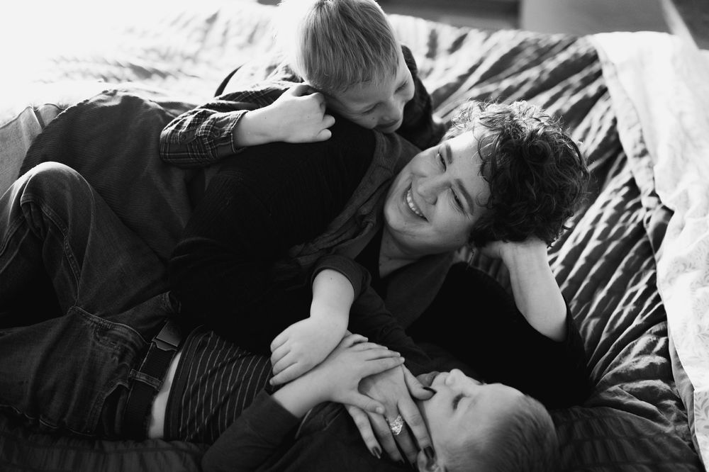 A black and white photograph shows three people lying together on a couch in a casual, relaxed pose.