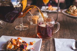 Tea being poured from a glass teapot to a glass teacup amongst a table setting for afternoon tea.