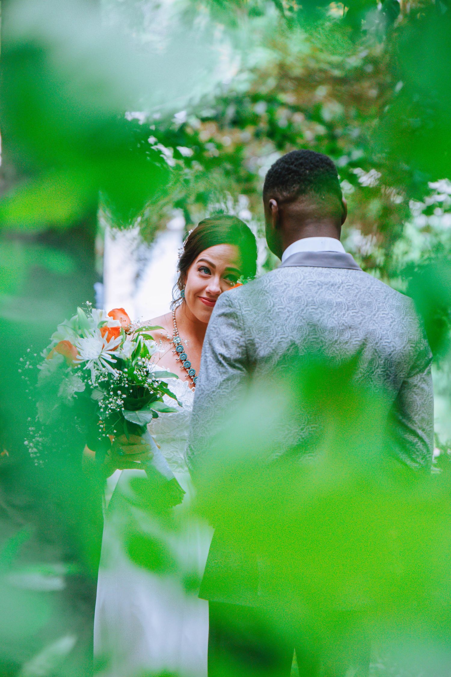 A couple shares a romantic moment in a green garden setting during their wedding celebration.