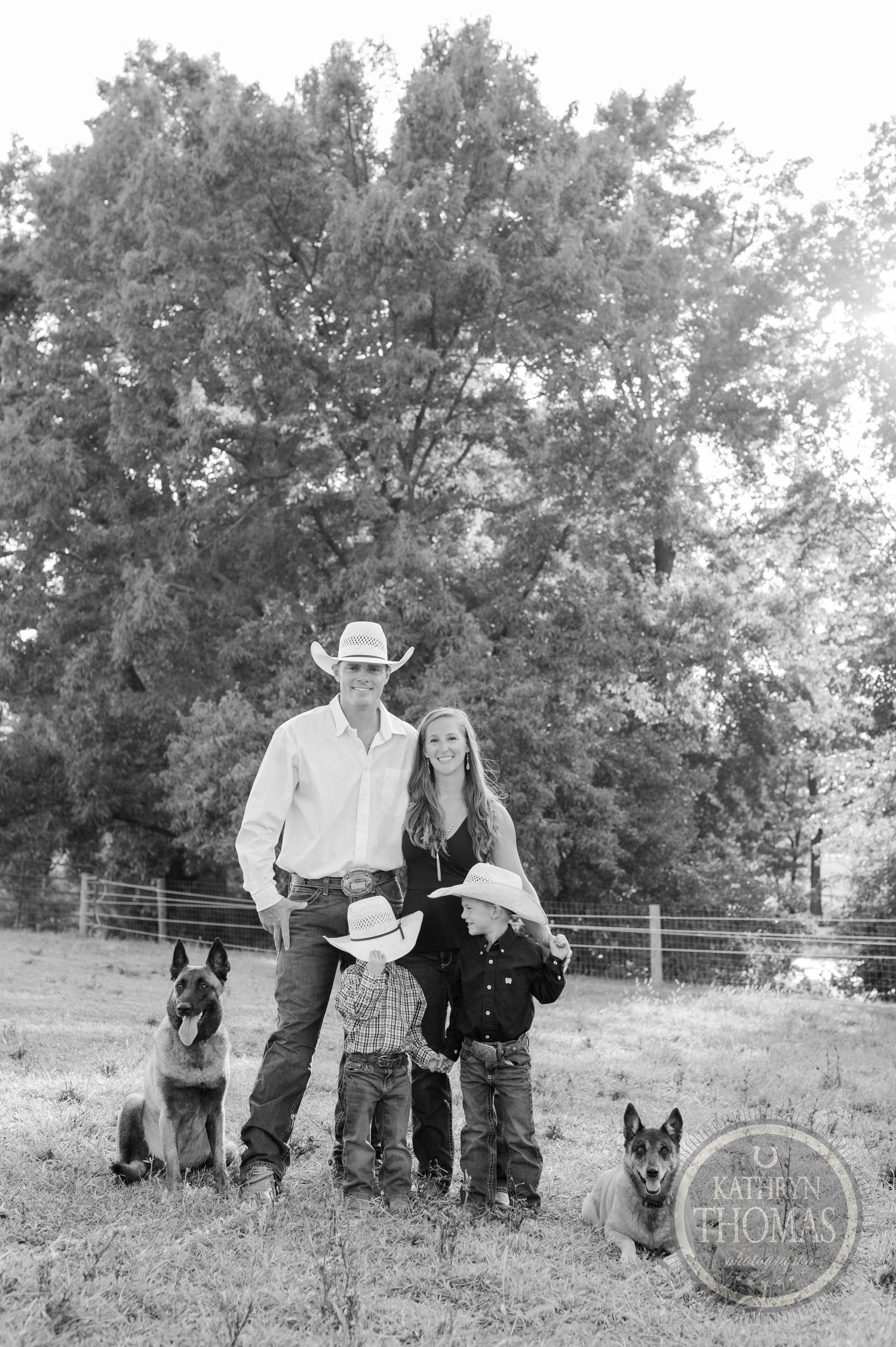 A rustic family portrait with German Shepherd dogs standing in a grassy field with trees in the background.