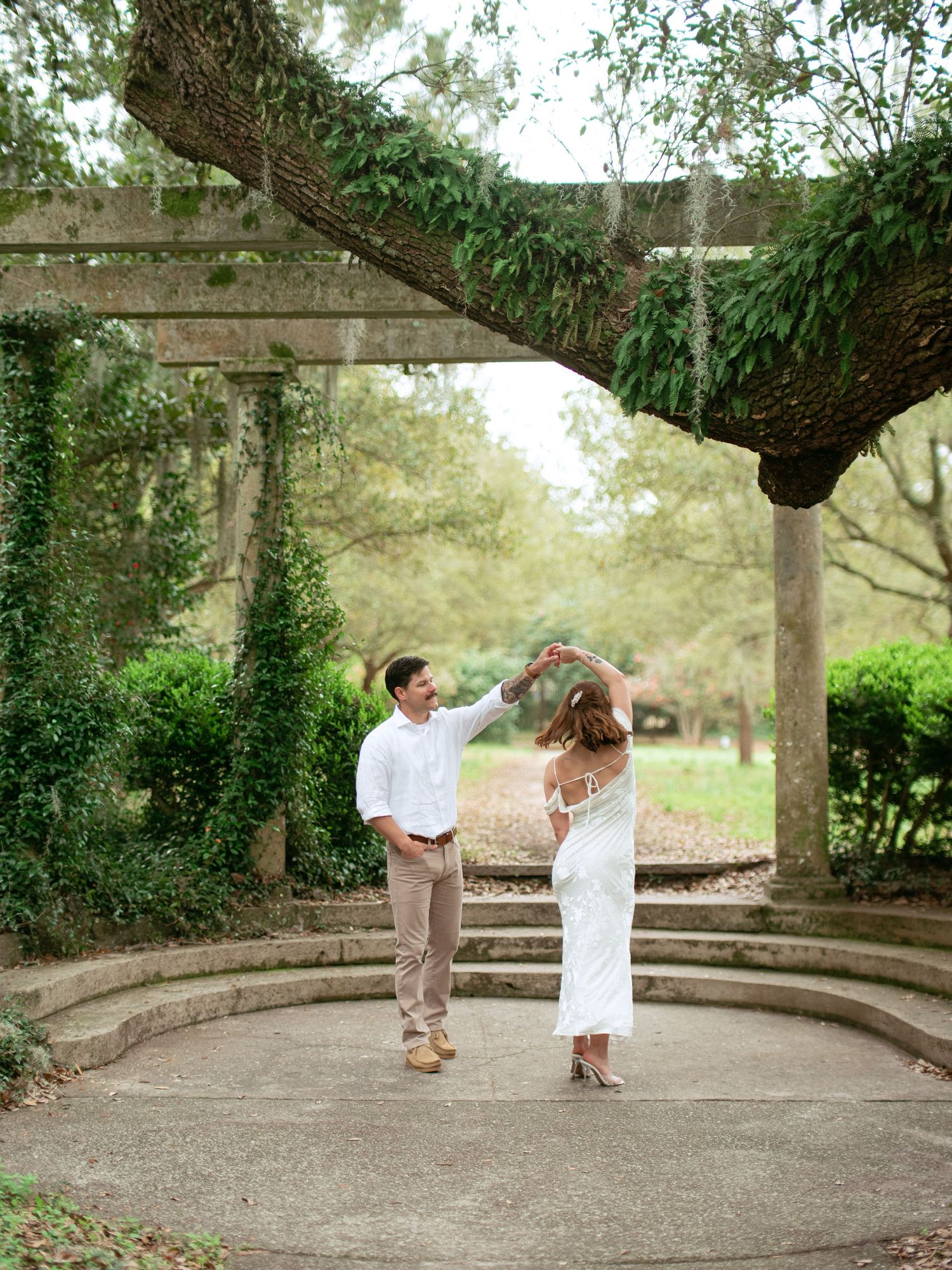 Dancing couple sharing a romantic moment under a vine-covered archway in a garden setting during golden hour.