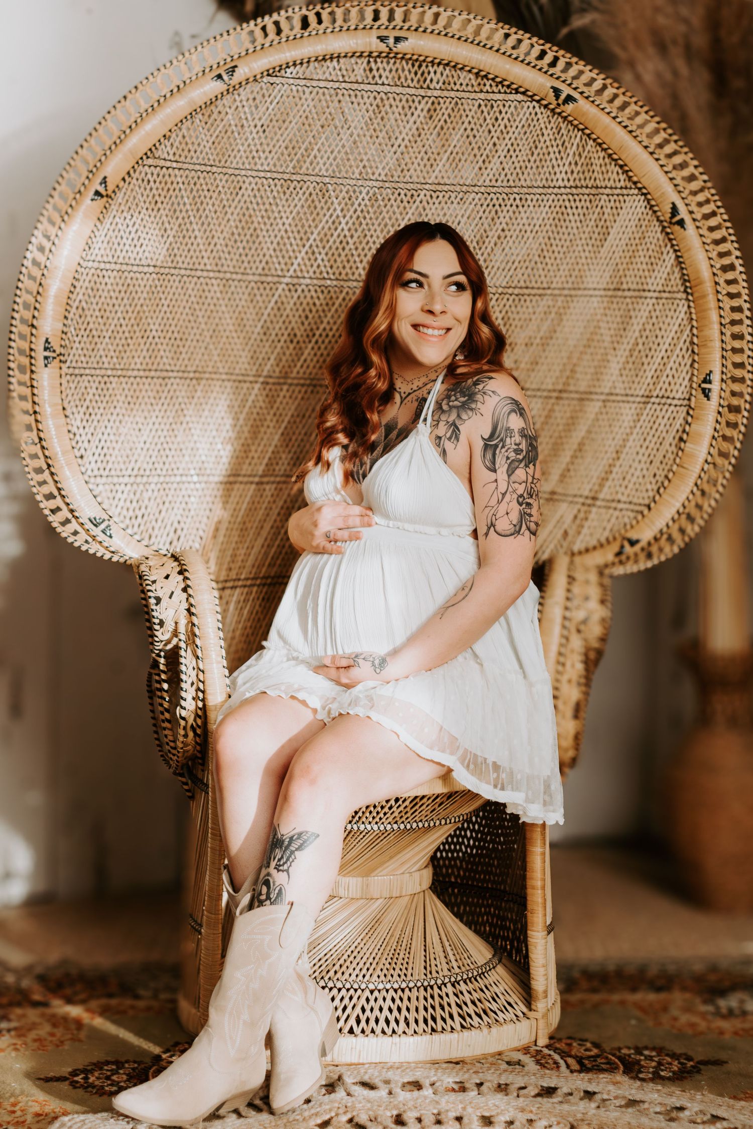 A person in a white dress sits on a peacock chair, wearing cowboy boots with visible tattoos.