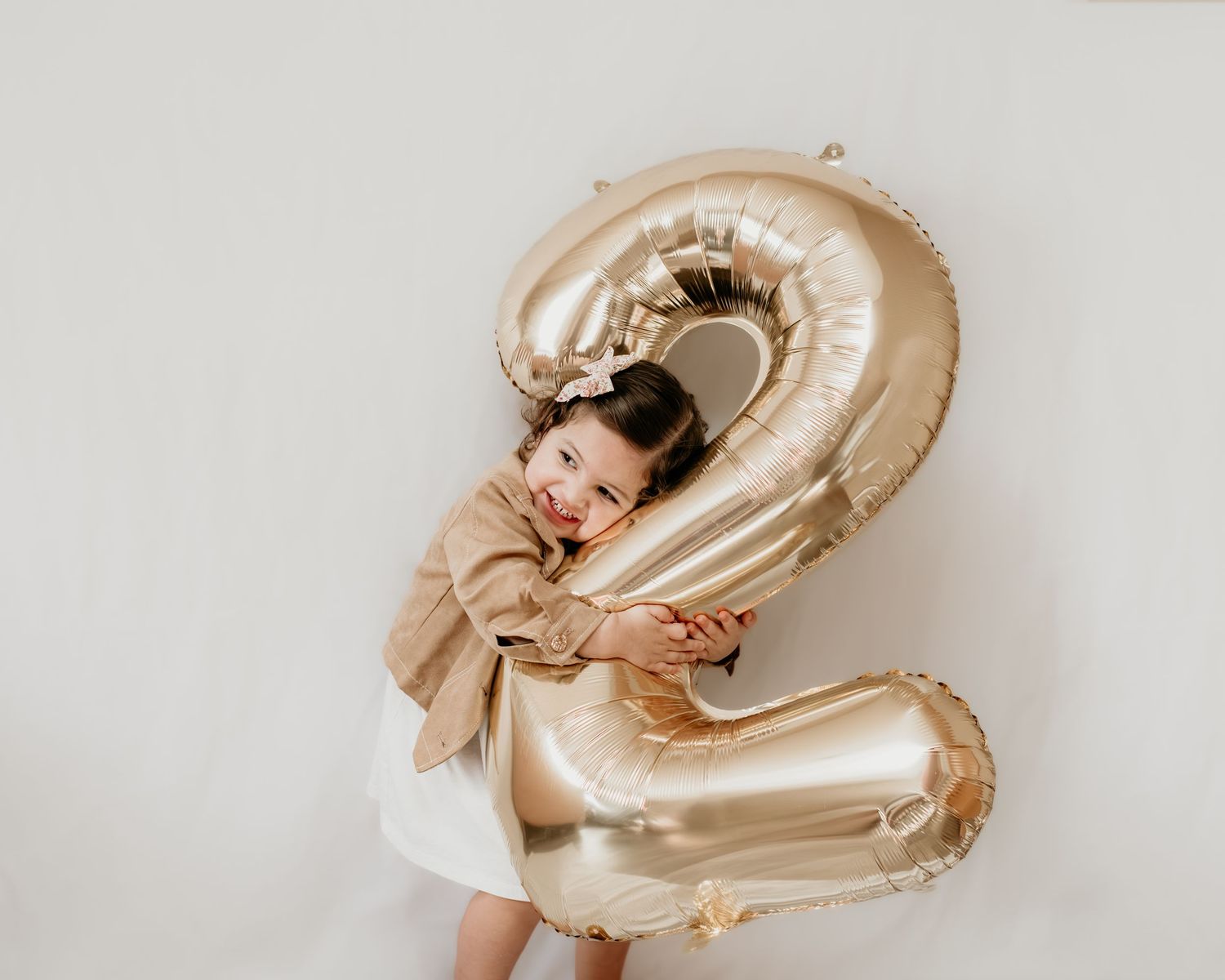 A large golden metallic number 2 balloon stands out against a white wall in a celebratory setting.