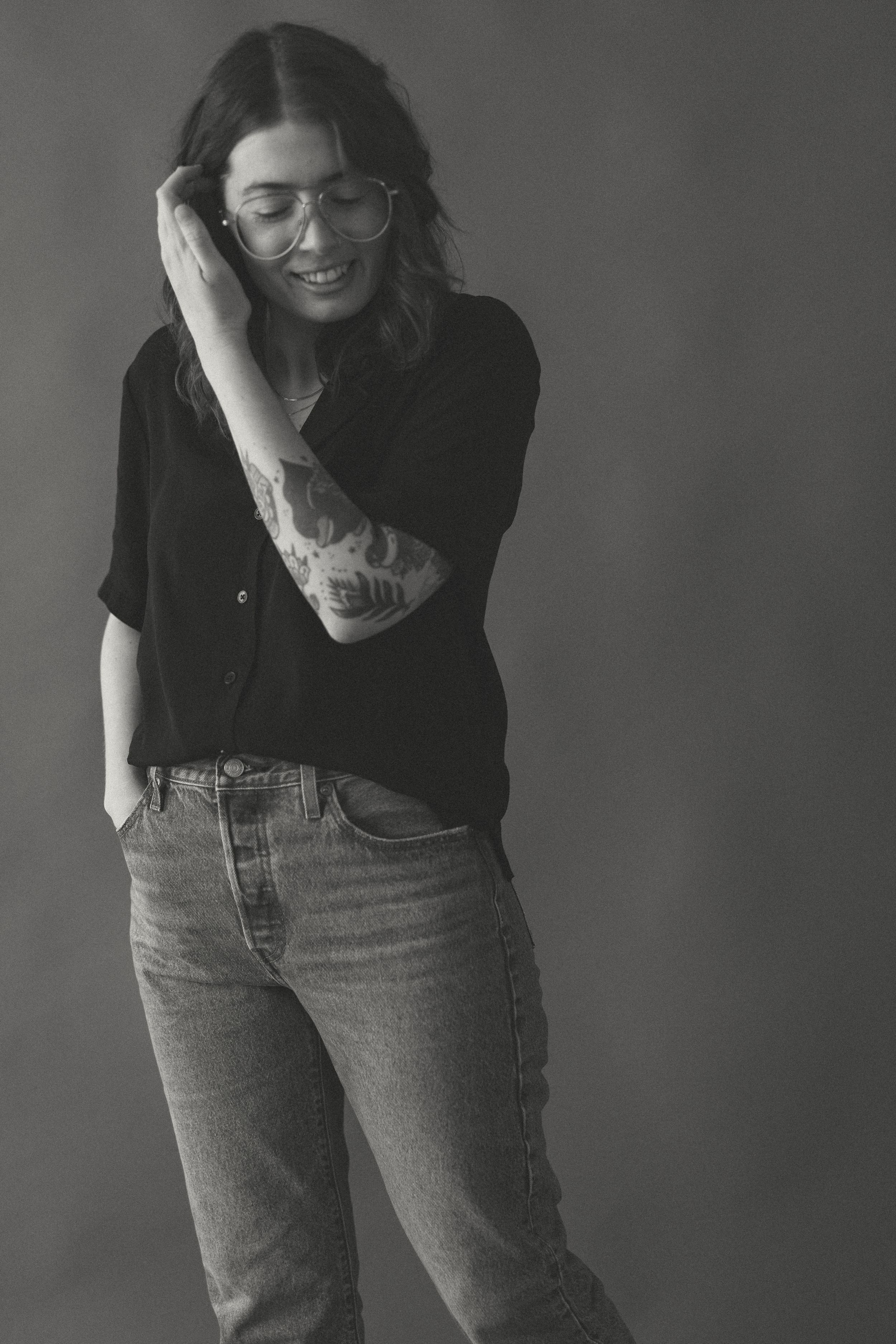 Person in black shirt and jeans laughs while touching their face in studio portrait.