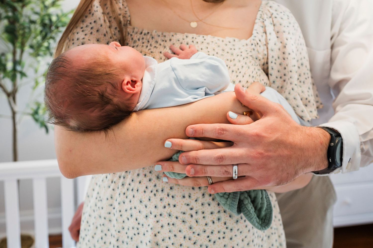 A mother in a polka dot dress cradles and feeds a small baby while sitting in a nursery room.